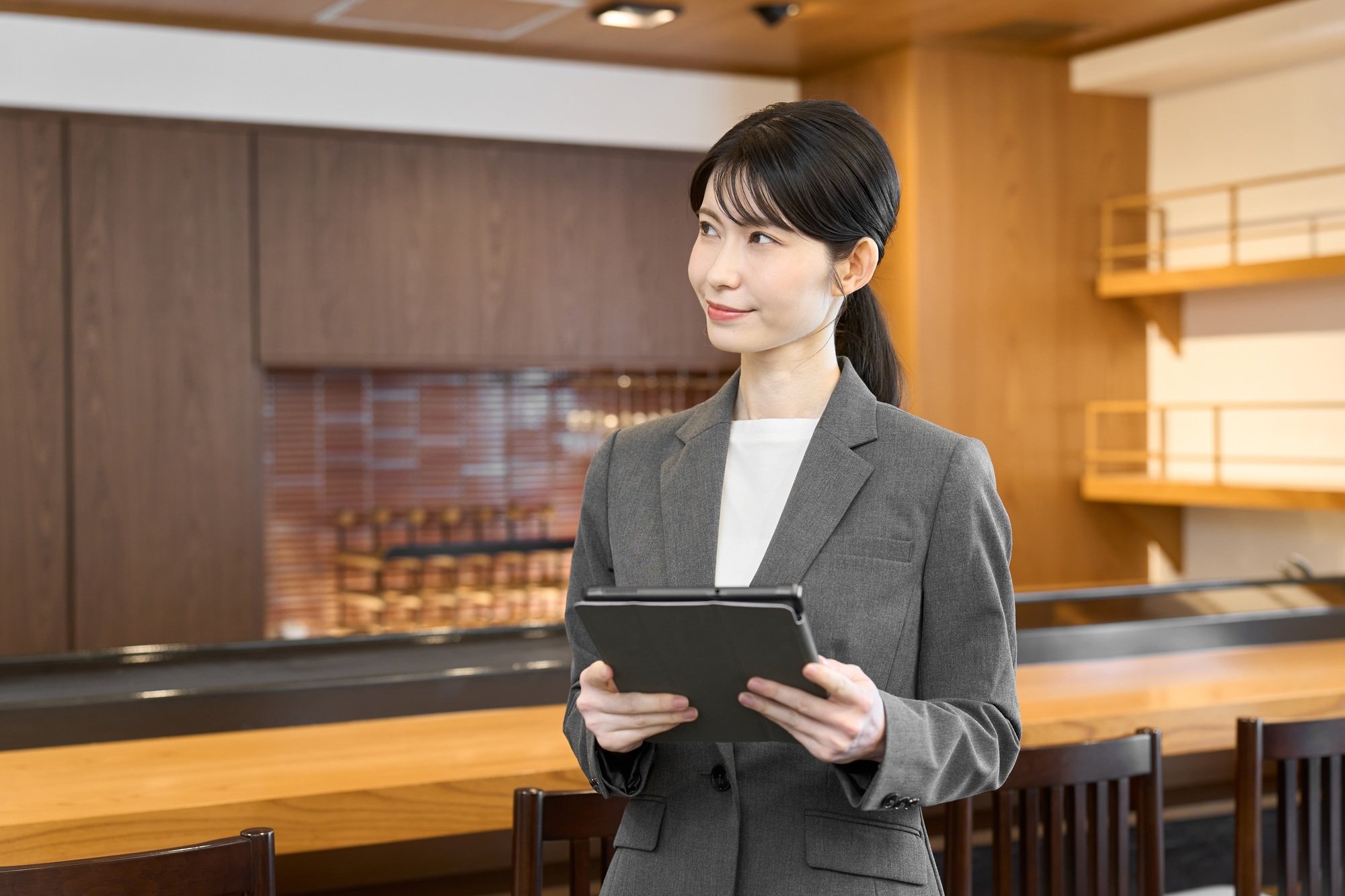 A woman in a suit holding a tablet and looking inside the store