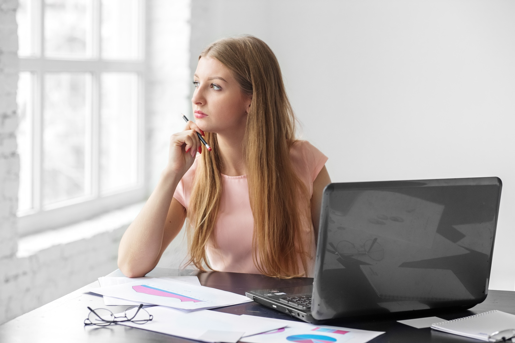 A young adult woman sits and thinks at a desk. The concept of business, work and making money.