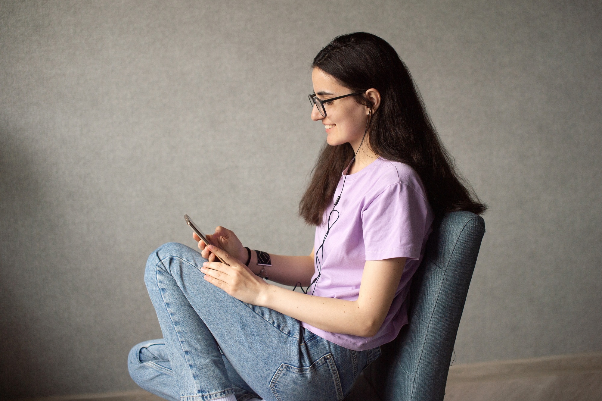 A young girl is sitting and looking at the phone with headphones