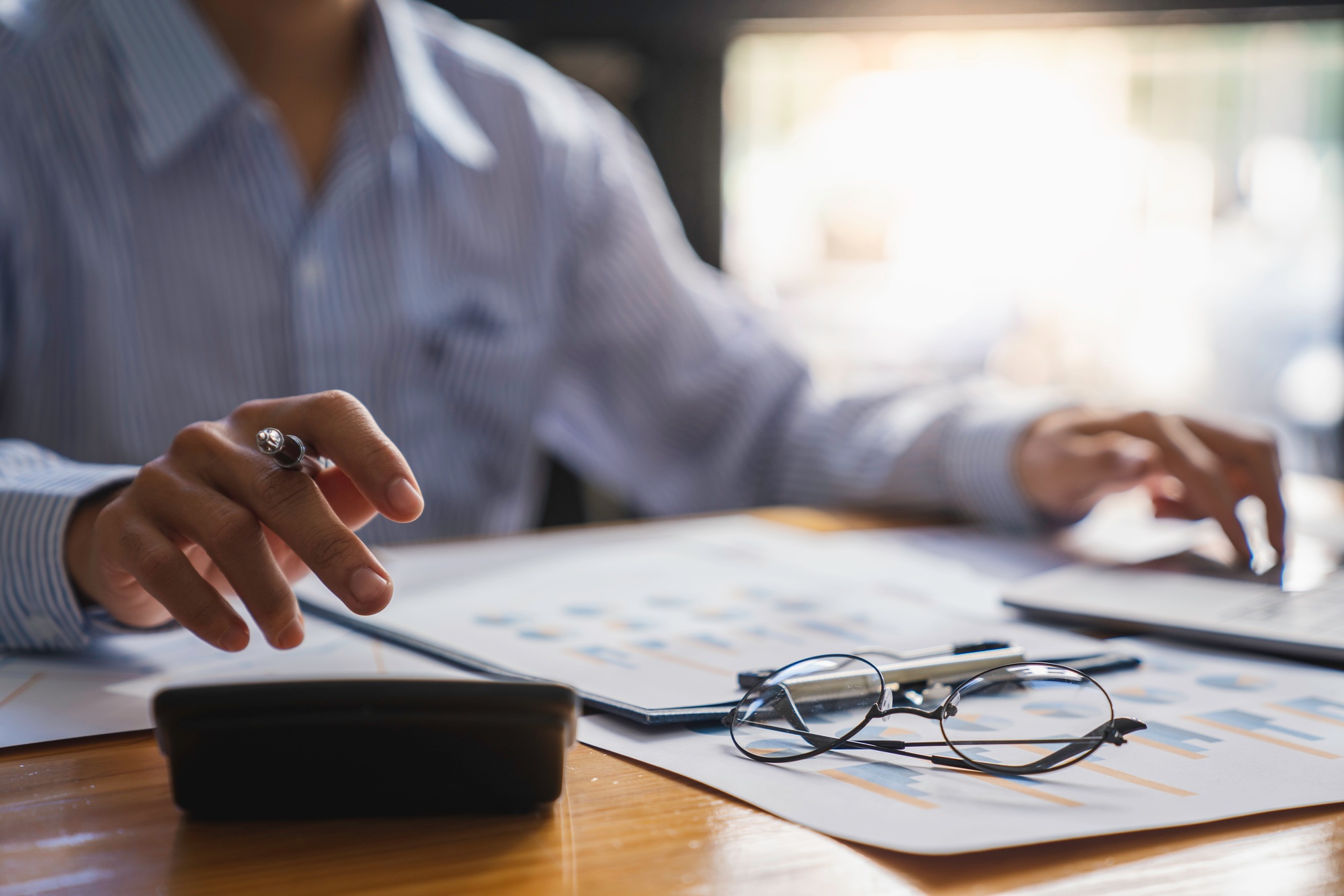 Accountant Or Financial Advisor Calculating Tax Using Calculator And Business Invoice On Wooden Desk