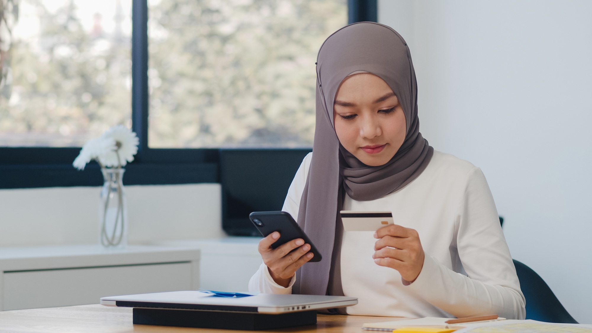 Asia muslim lady using phone, credit card buy and purchase e-commerce internet in office.