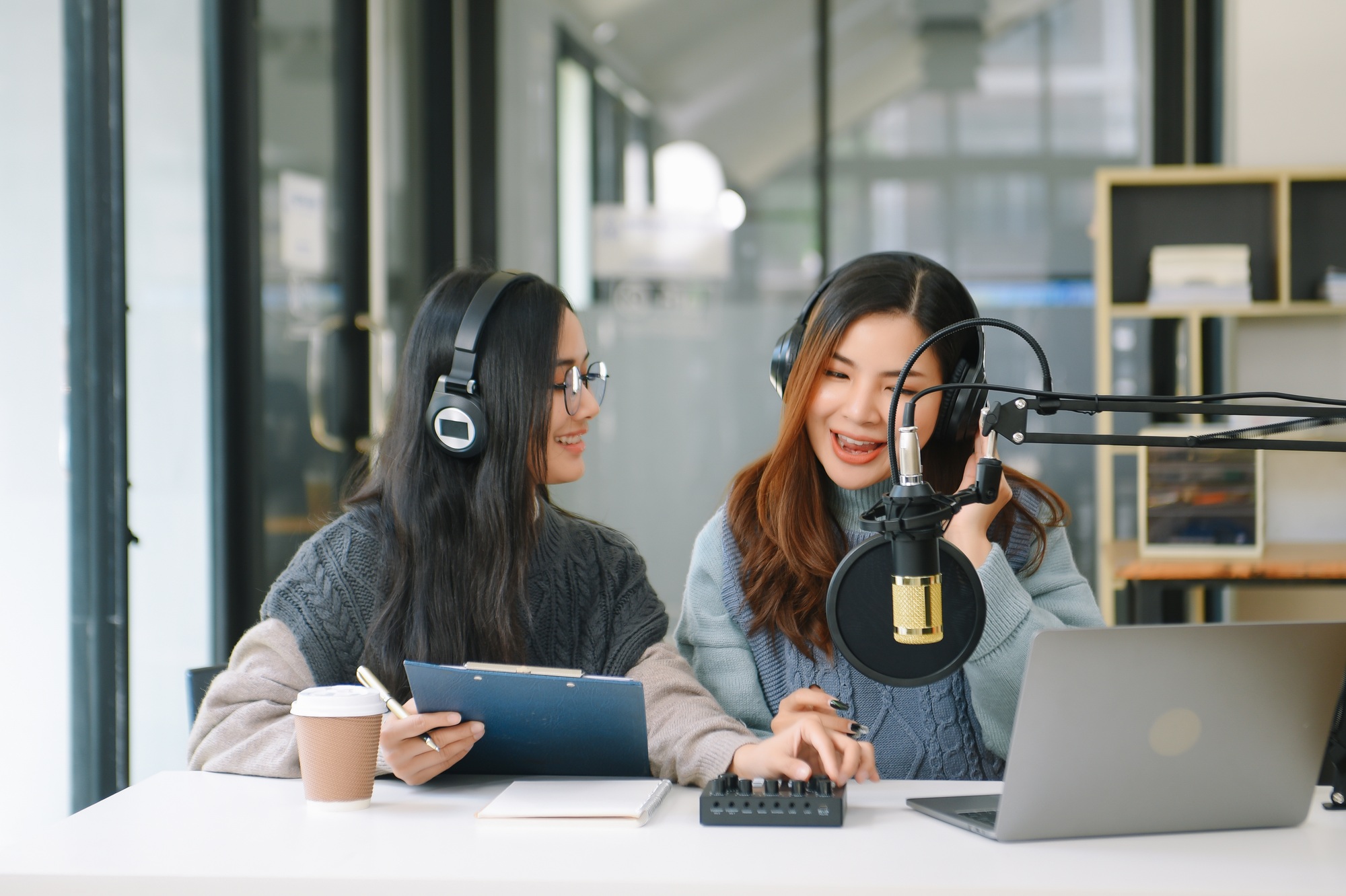 Asian woman use microphones wear headphones with laptop record podcast interview for radio.