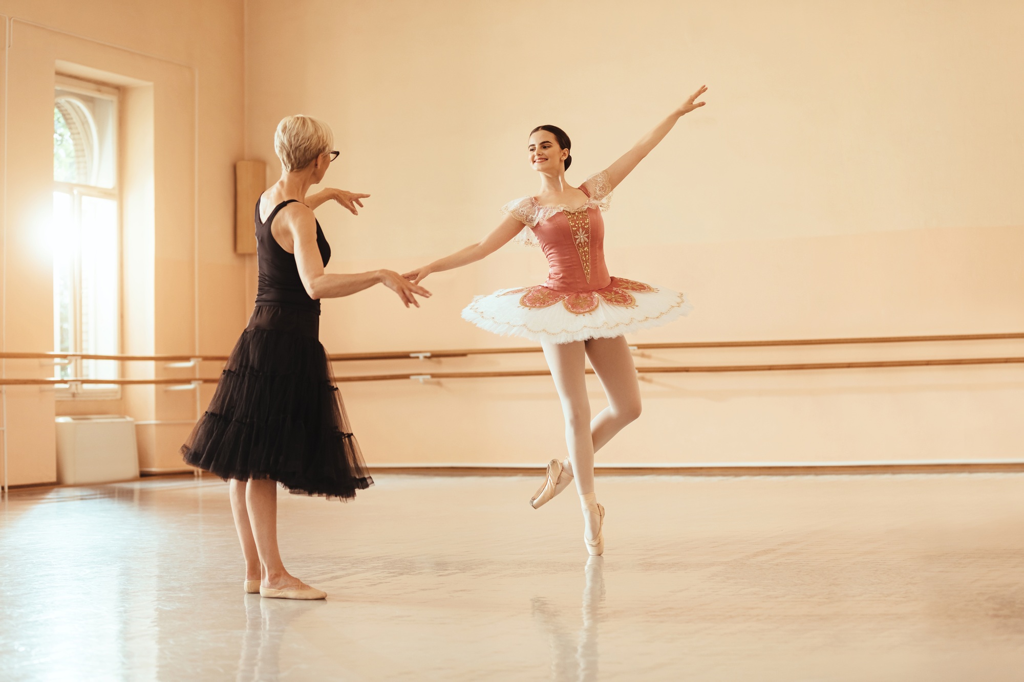 Ballet instructor teaching young ballerina in dance studio.