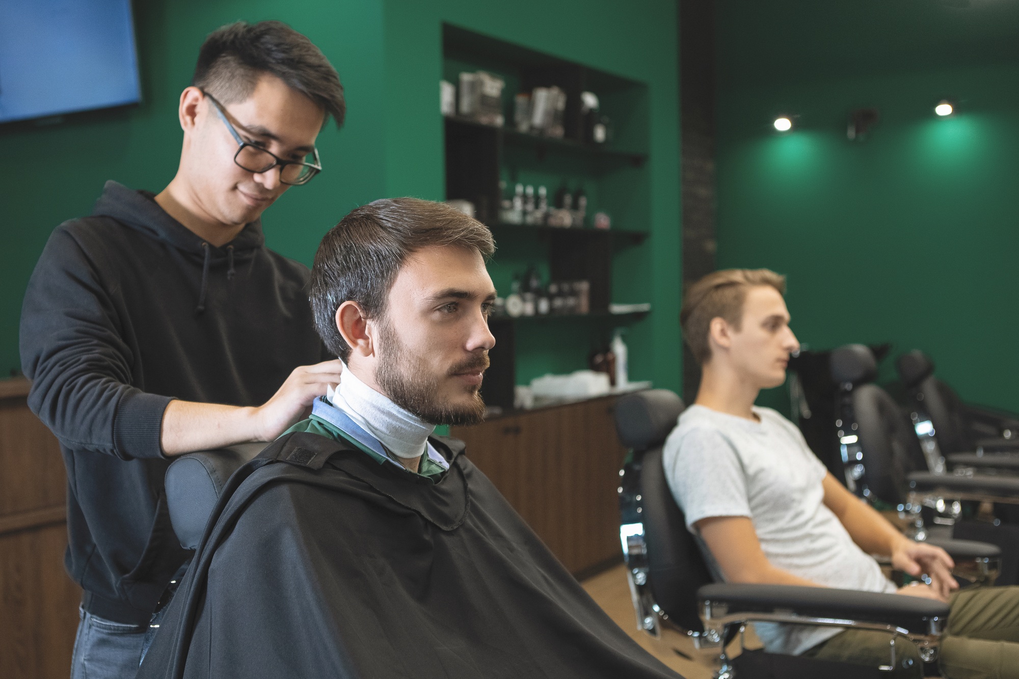 Bearded guy in a hairdressing chair in a barbershop salon with a master.