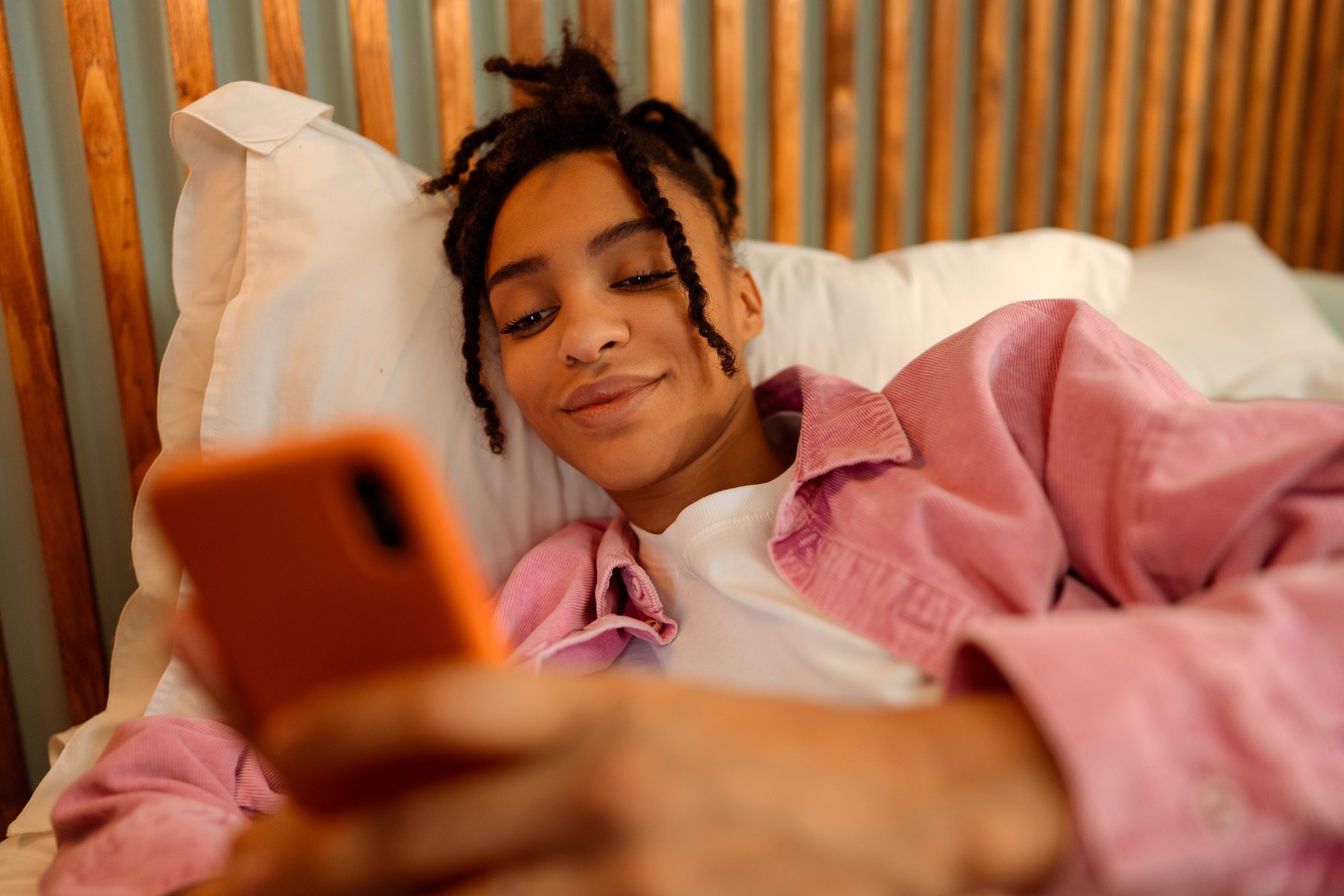 Beautiful African America lying on bed at home holding mobile phone, using mobile application