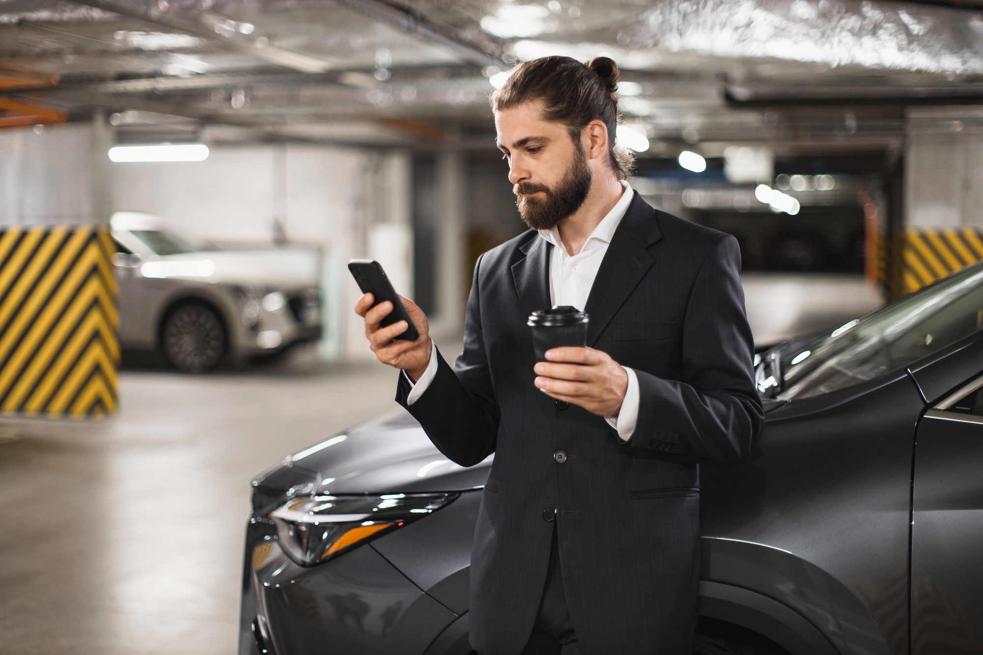 Businessman using phone while holding coffee in car parking lot