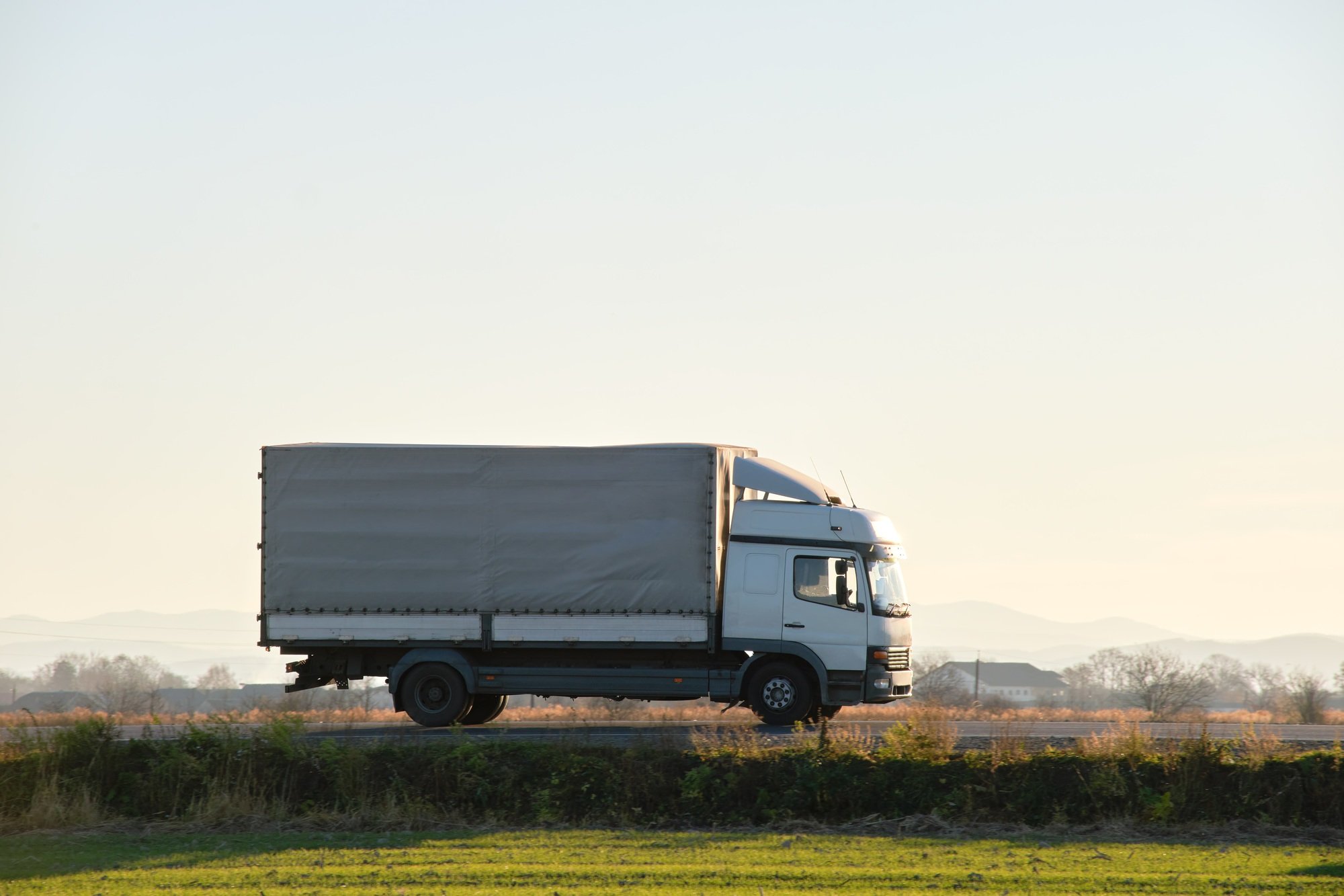 Cargo truck driving on highway hauling goods in evening.