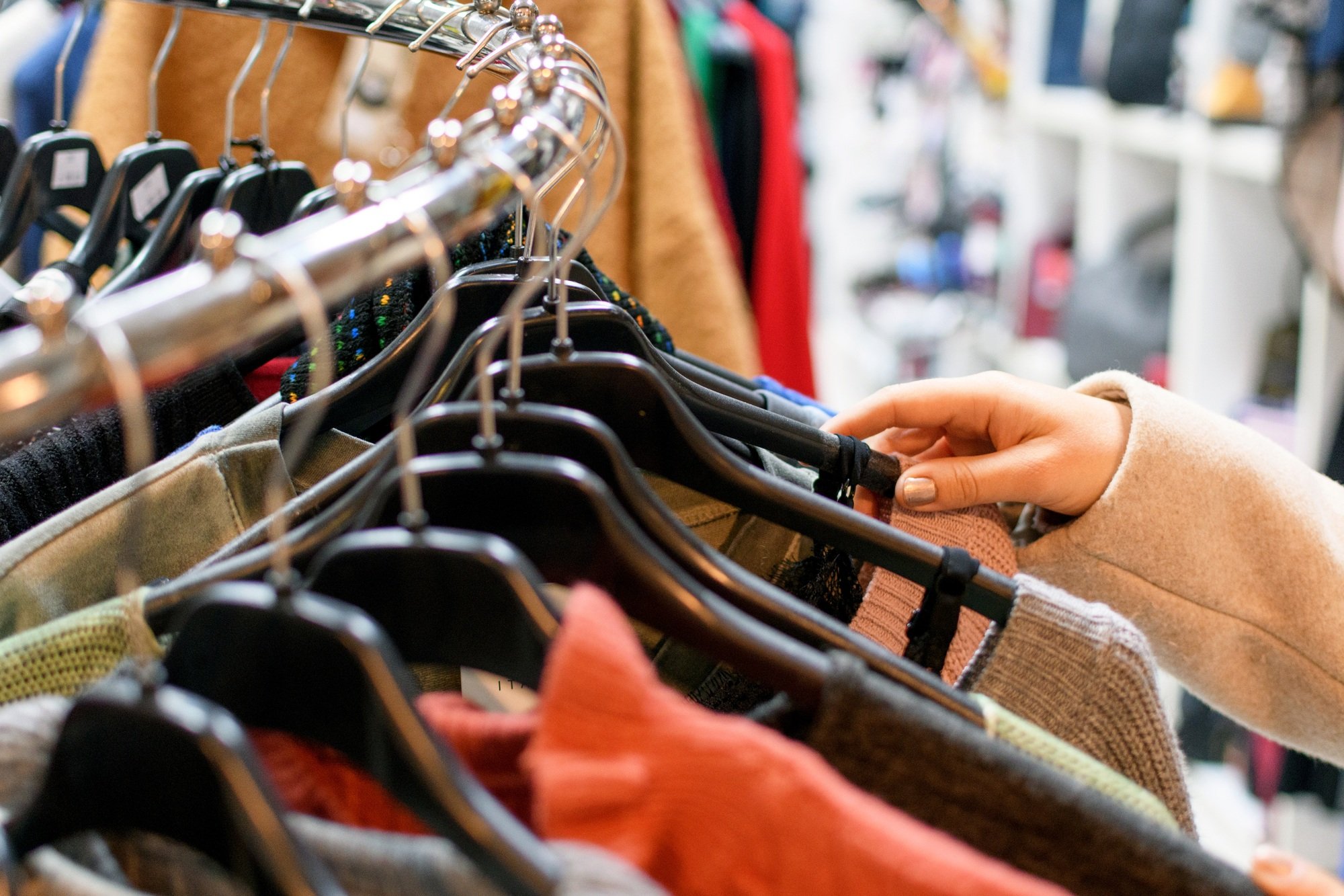 Close-up selective focus image of woman looking at clothes on hangers in store.
