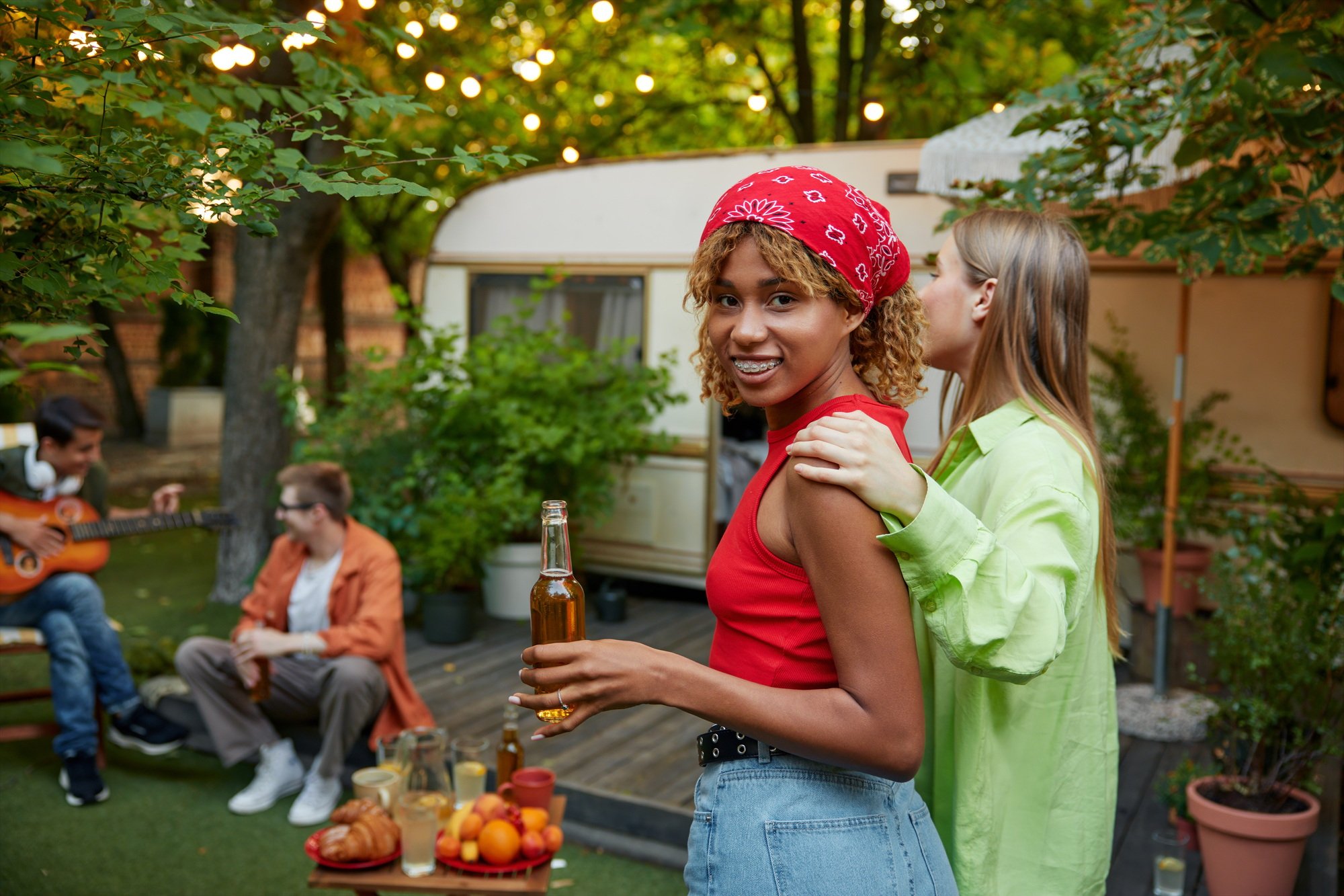 Company of millennial friends having party at picnic site in woods