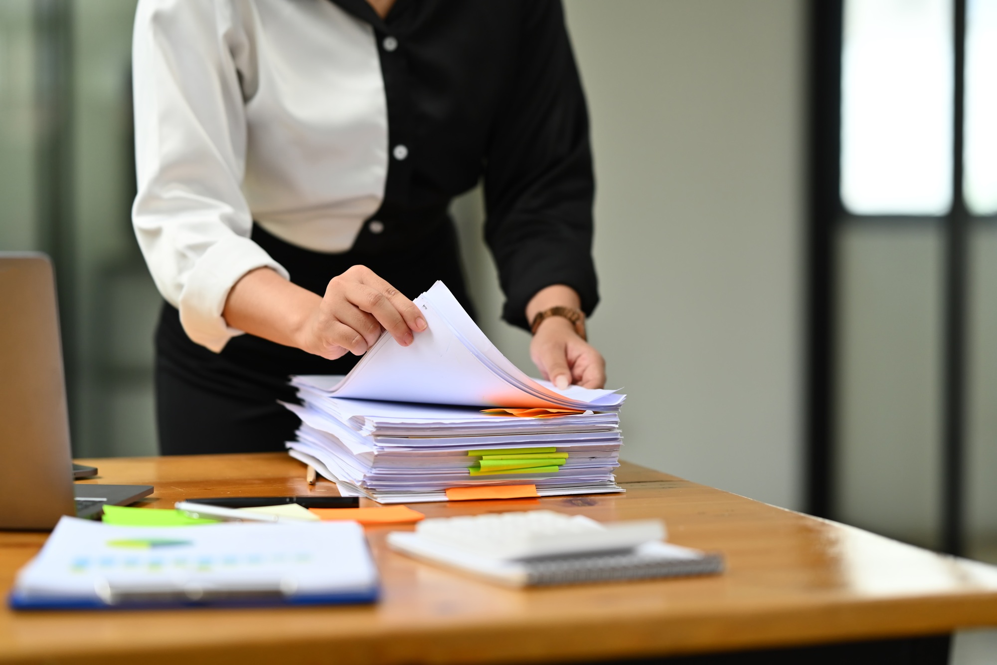 Cropped image of female bookkeeper checking unfinished accountancy report on wooden office desk.