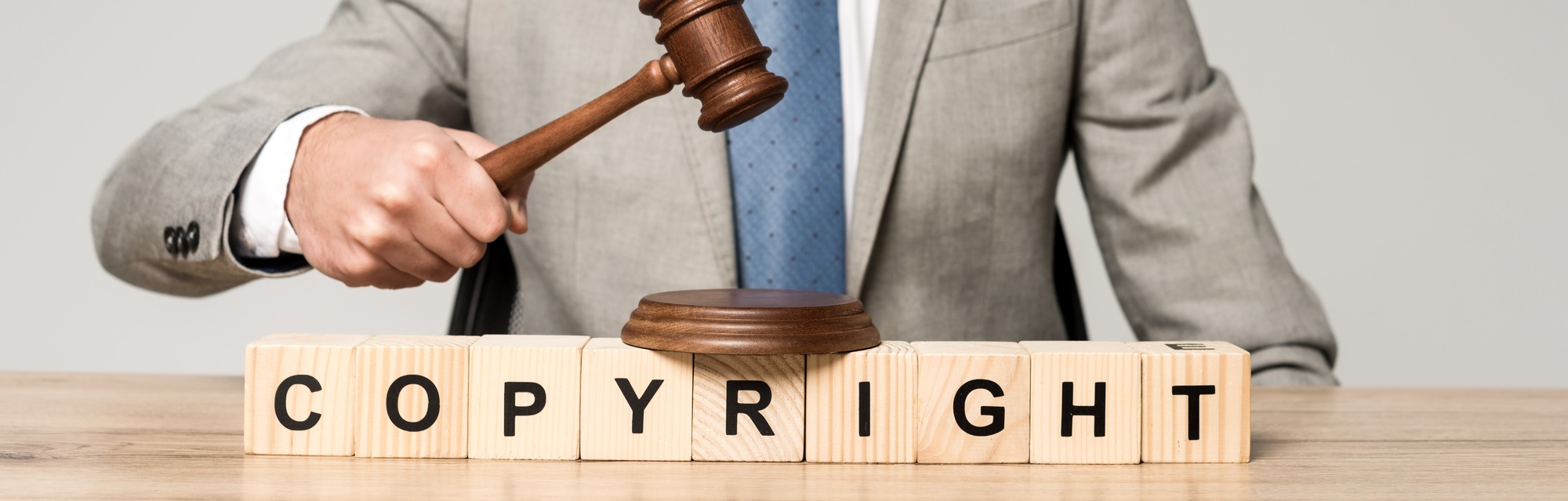 cropped view of judge holding gavel near wooden cubes with copyright inscription isolated on grey,