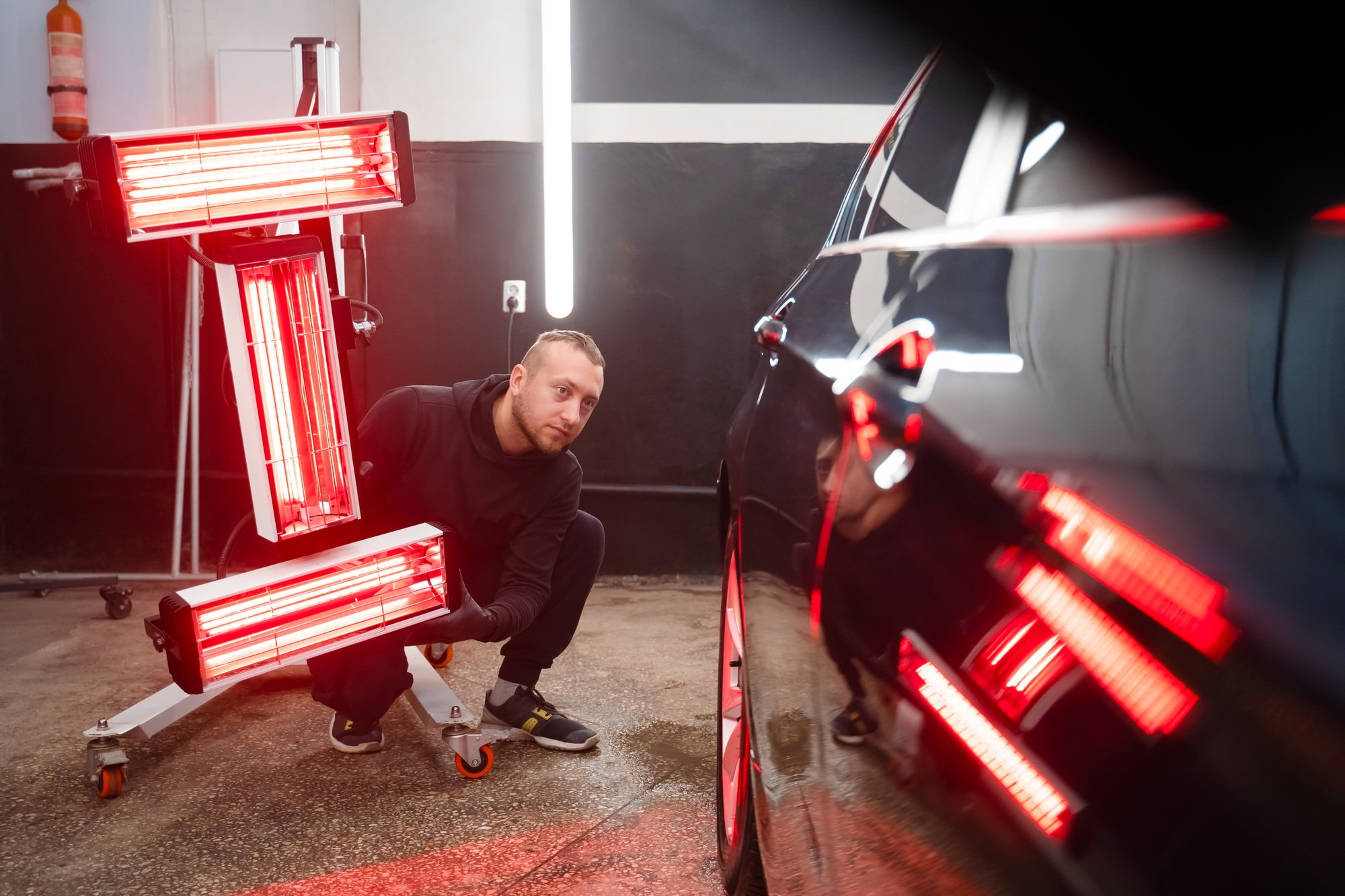 Detailing worker with infrared lamps near the car. Car detailing concept