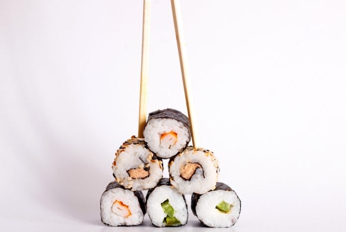 Eating Sushi with chopsticks. Sushi roll japanese food in restaurant isolated on white background.