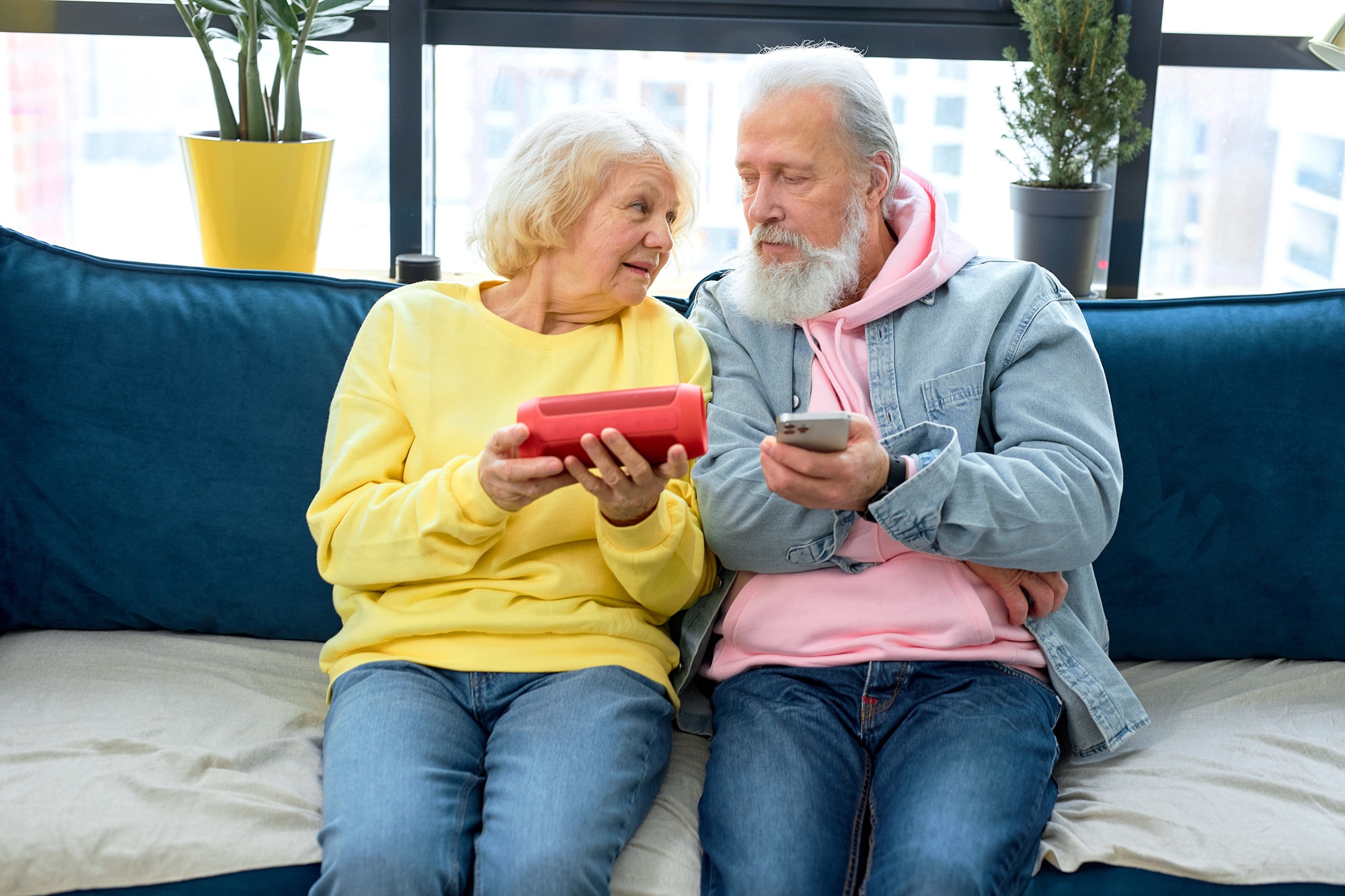 Excited senior couple using a Virtual Assistant music loud speaker at home, having fun