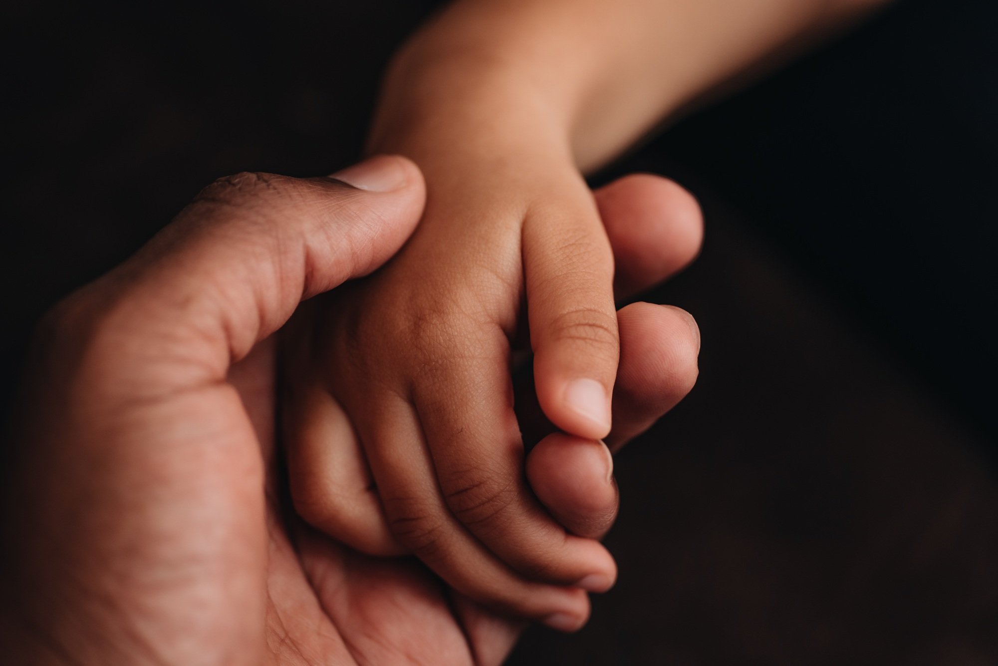 Farher holding daughters hand in act of kindness against dark background