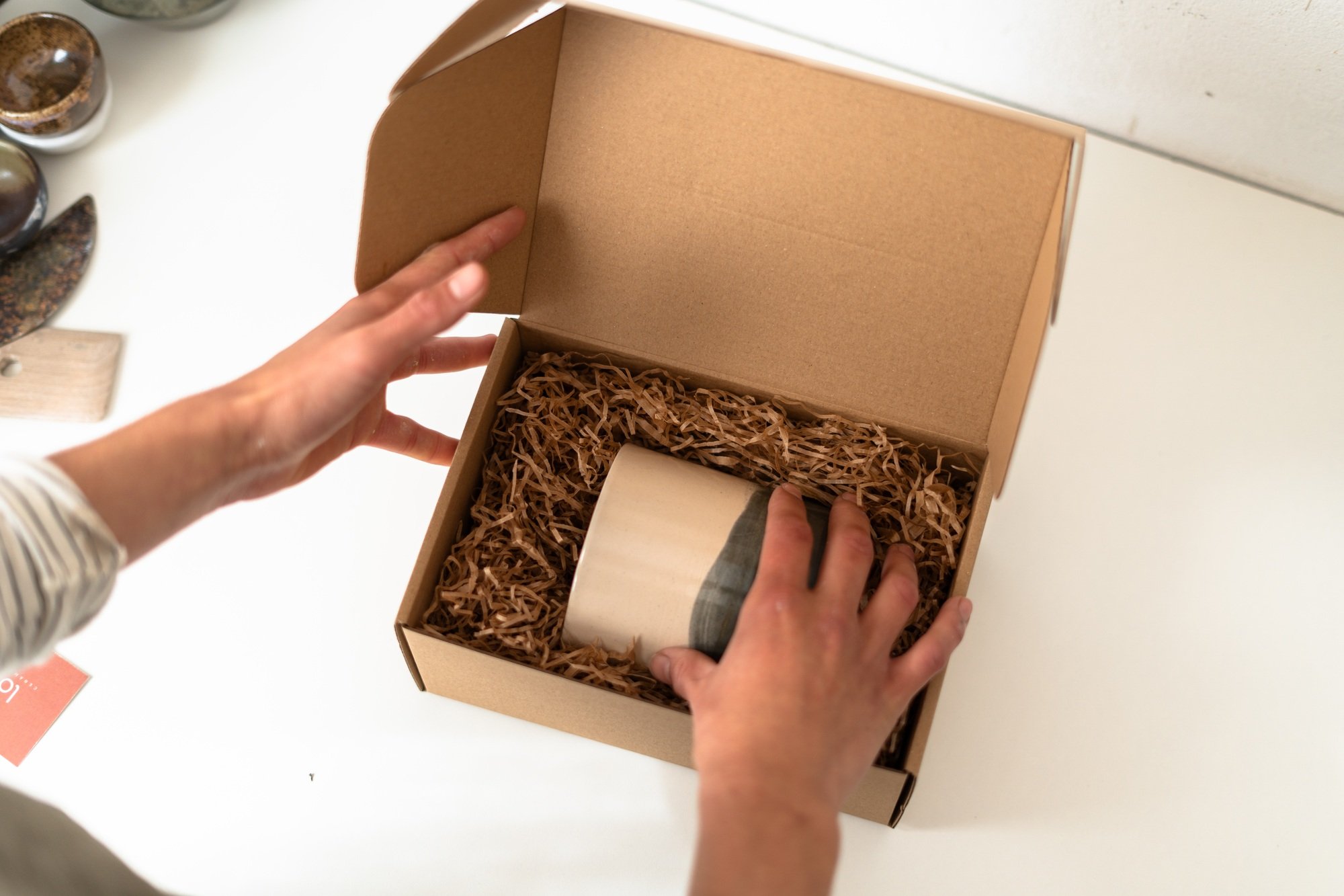 Female ceramic artist carefully packaging handmade mug for shipping