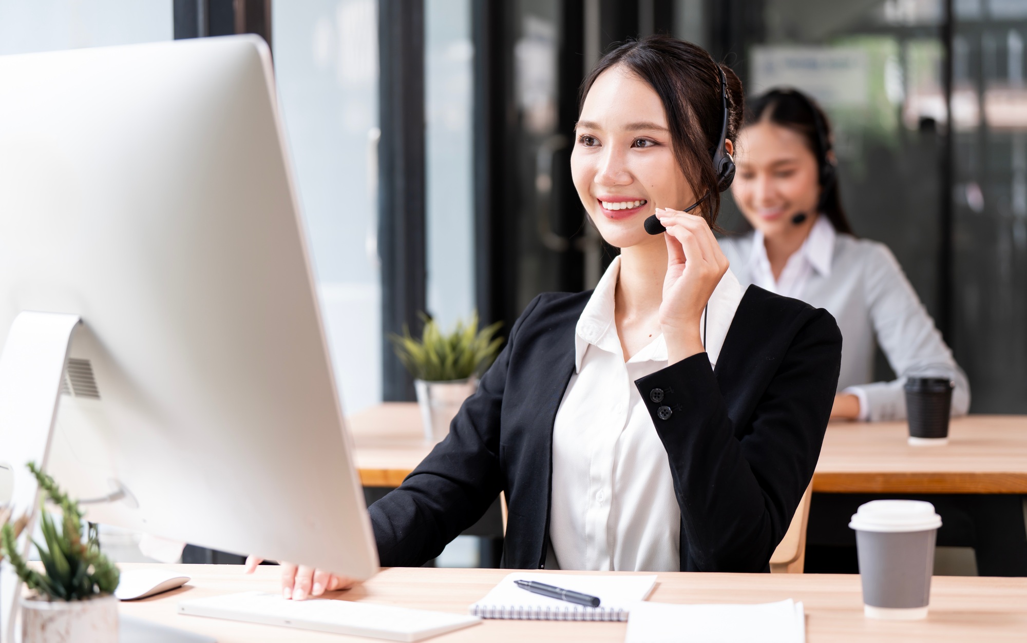 female customer service representative wearing a headset works at a computer in a modern office.