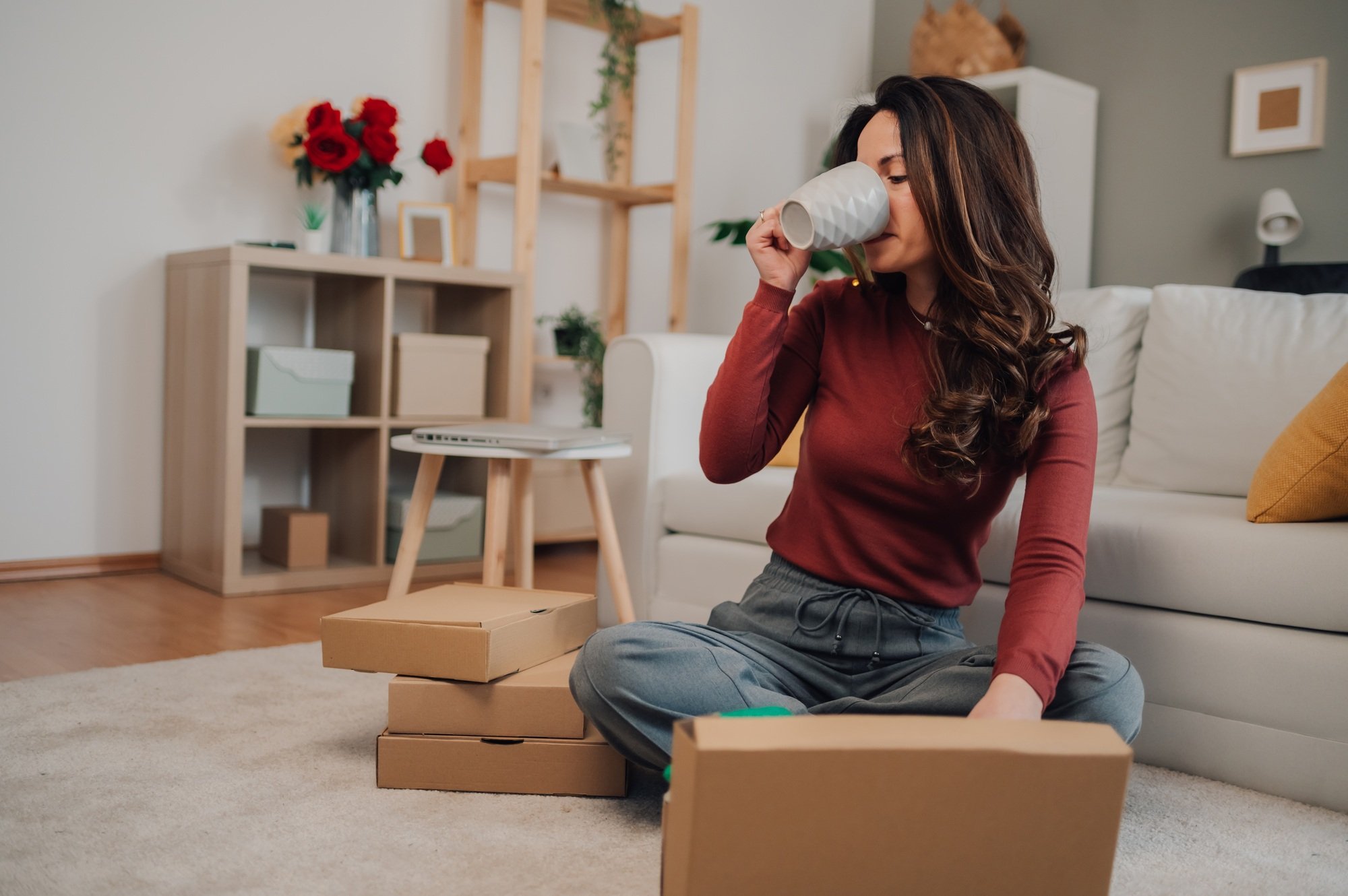 Female entrepreneur drinking coffee and preparing packages for shipping in home office