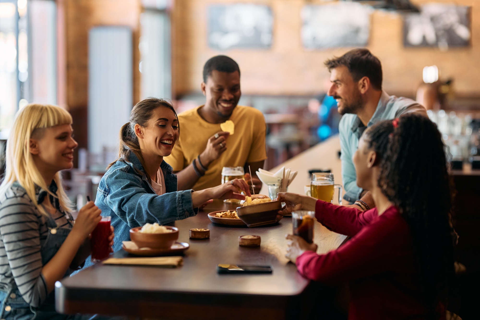 Group of happy friends having a snack while drinking in a bar.