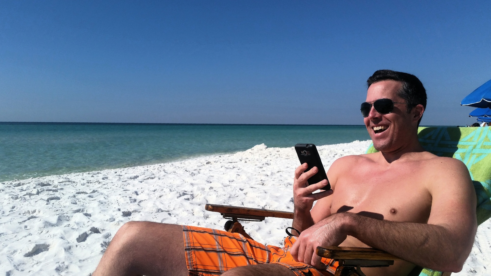 Hipster cool millennial relaxing on beach laughs at an Instagram post as happy people on vacation.