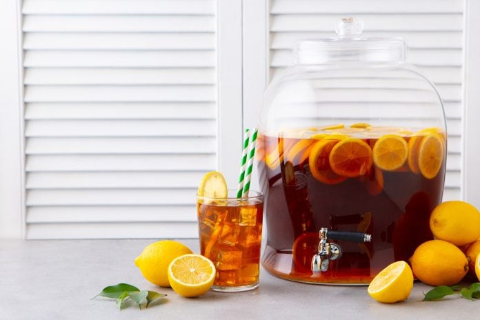Ice Tea, Lemonade in glass and beverage dispenser with fresh lemons. Grey background. Copy space.