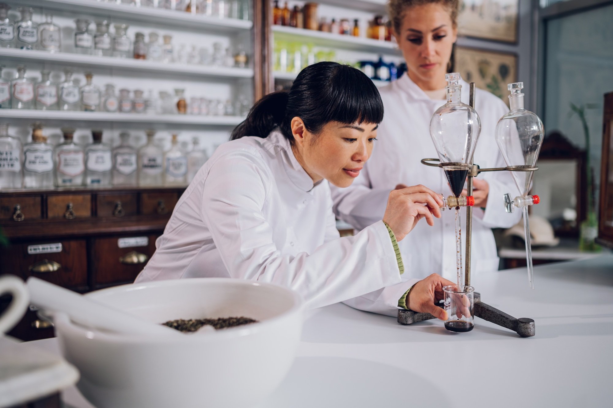 Interracial chemists are using lag equipment in a pharmacy and making new medicine.