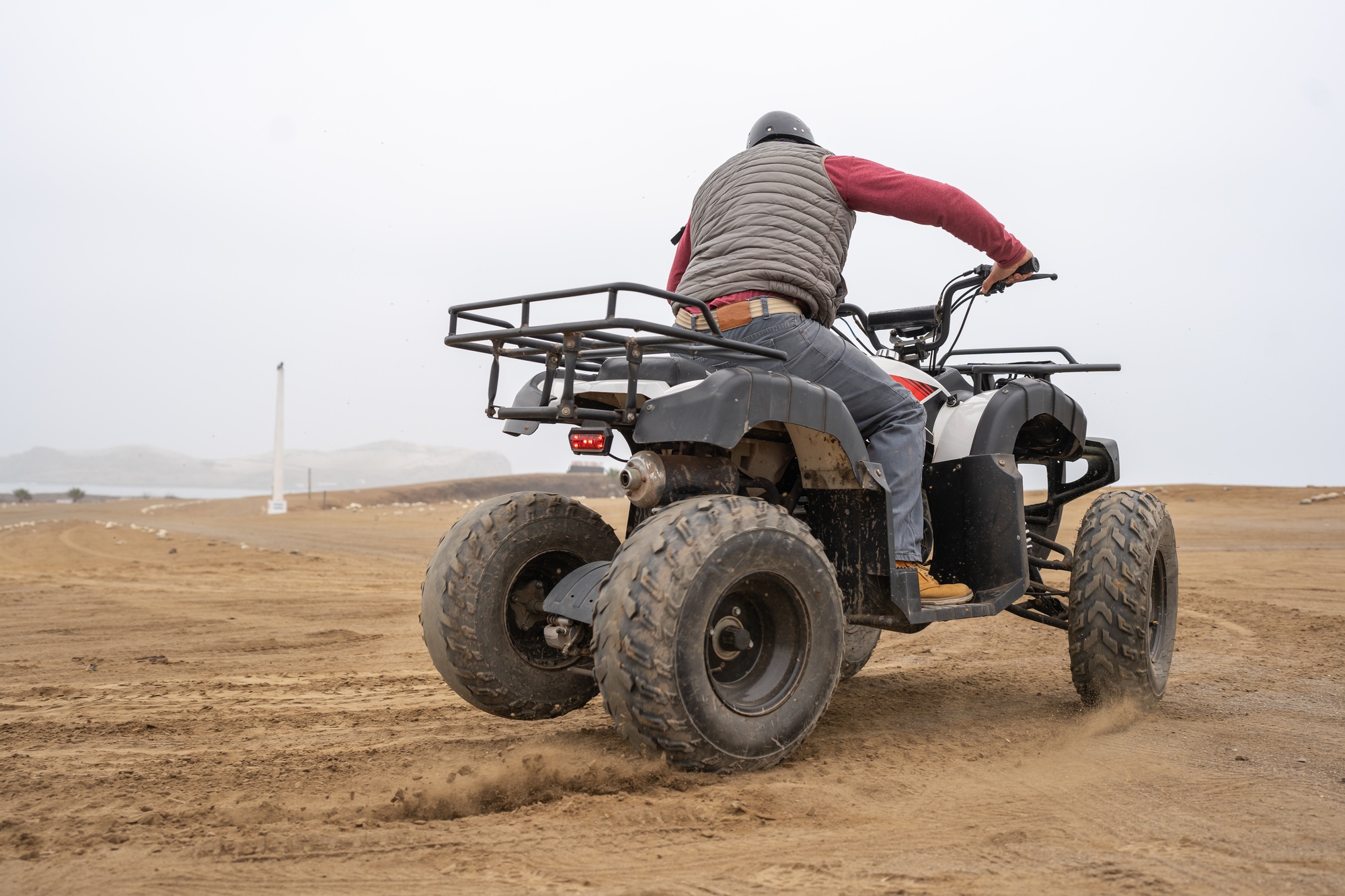 Man kicking up dust while driving a quad on a beach