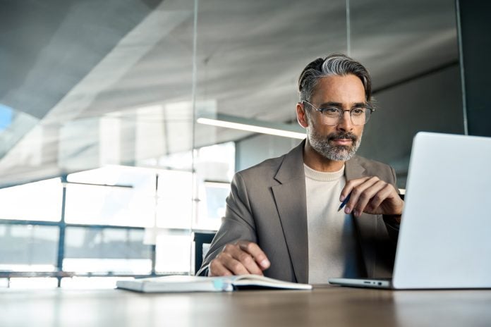 Mature busy businessman executive looking at laptop sitting at desk. Copy space.