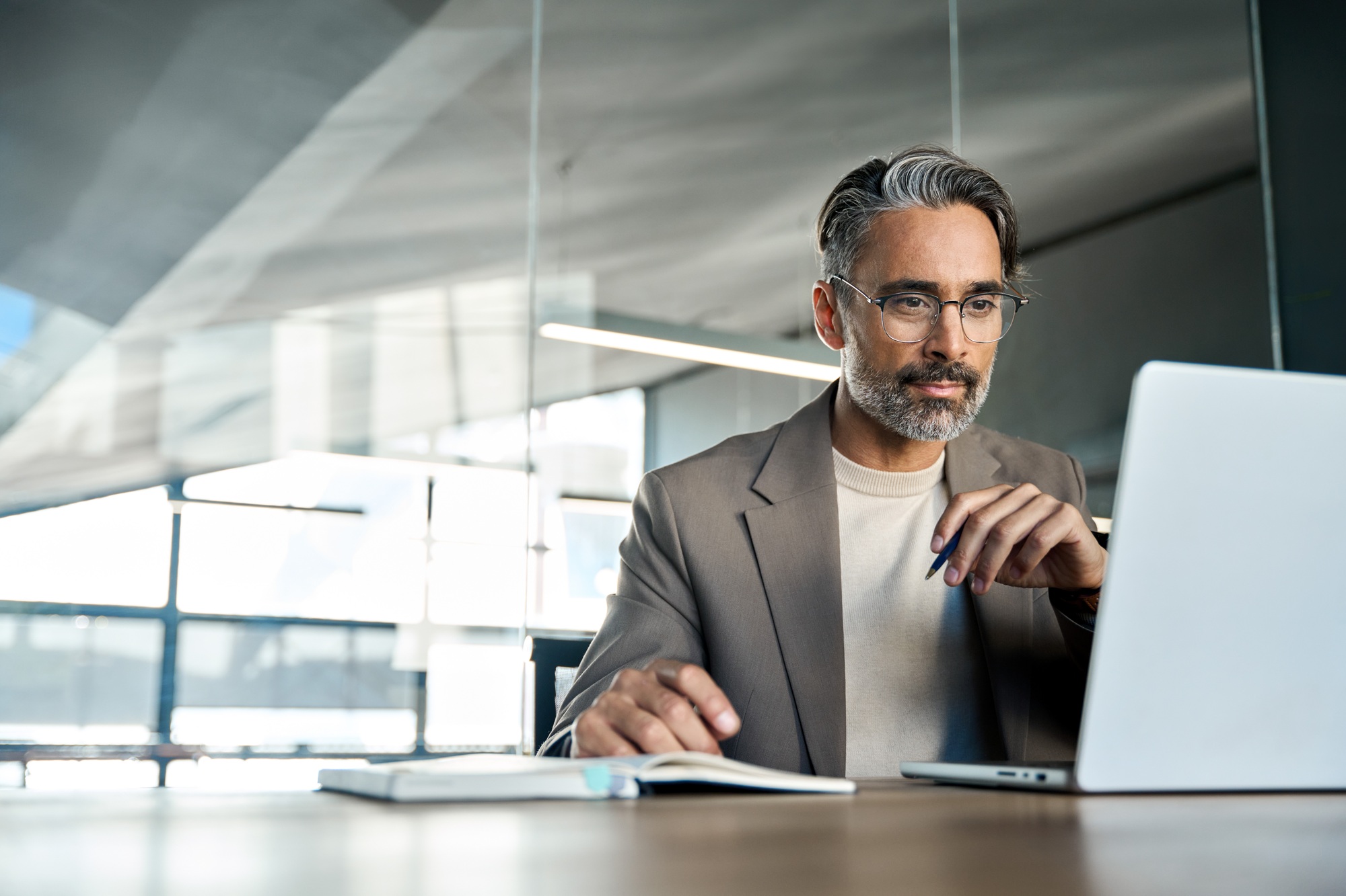 Mature busy businessman executive looking at laptop sitting at desk. Copy space.