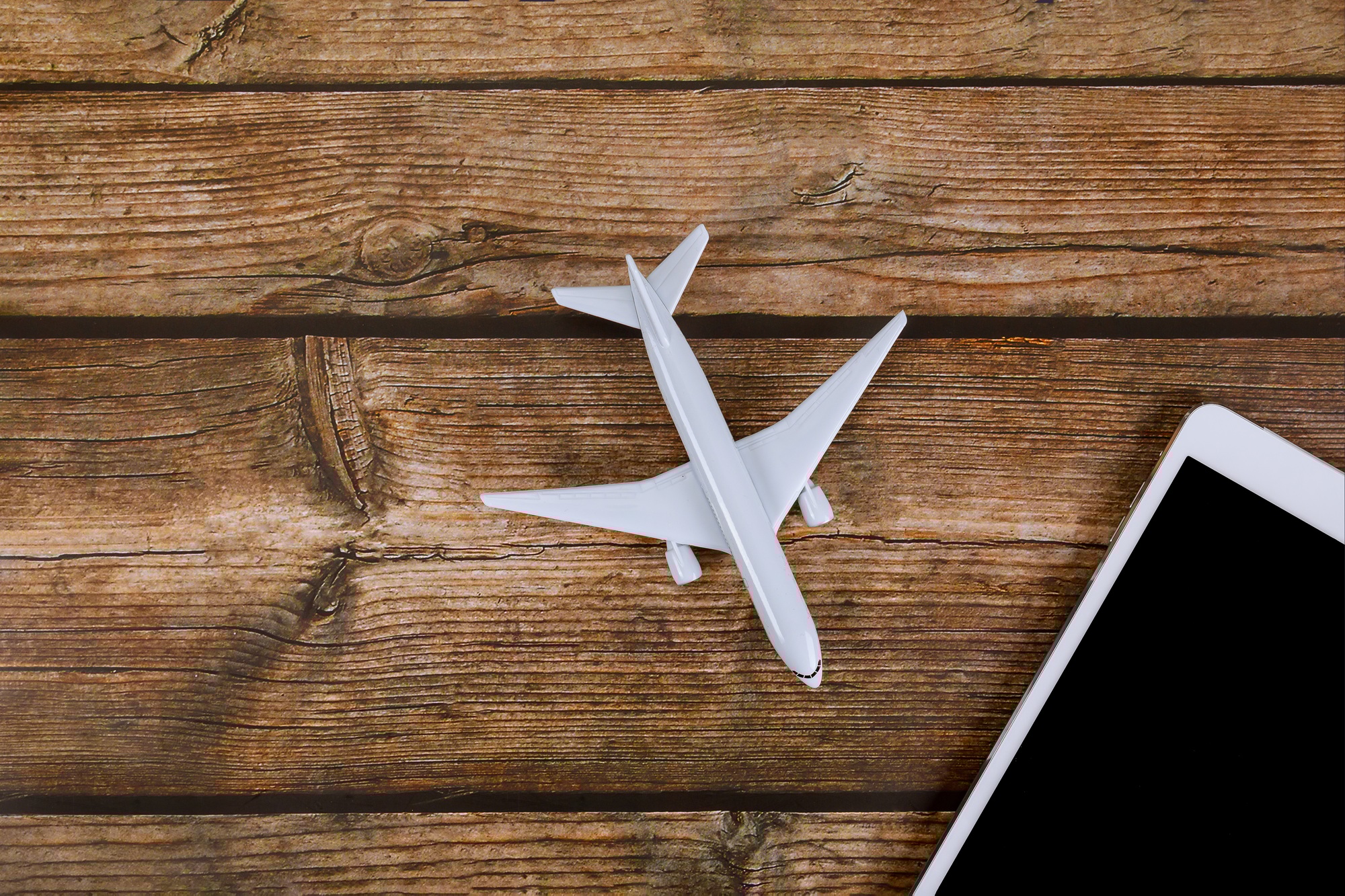 Miniature airplane, tablet on wooden surface creating travel technology theme with online ticket