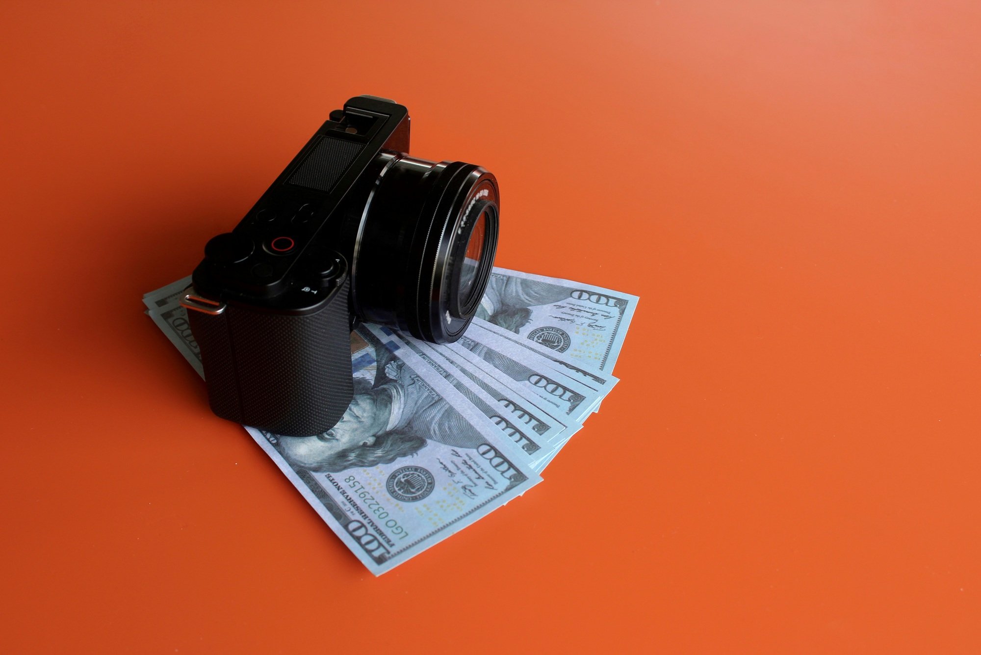 Mirrorless camera and money on orange background with copy space.