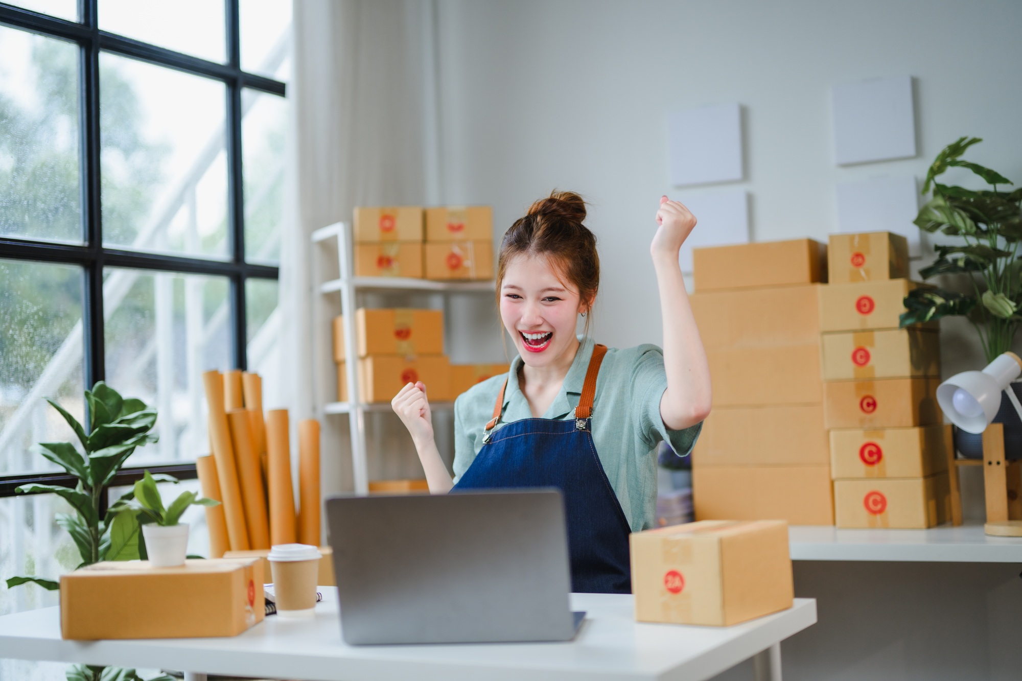 Online seller celebrating successful sales with laptop and packages in her office