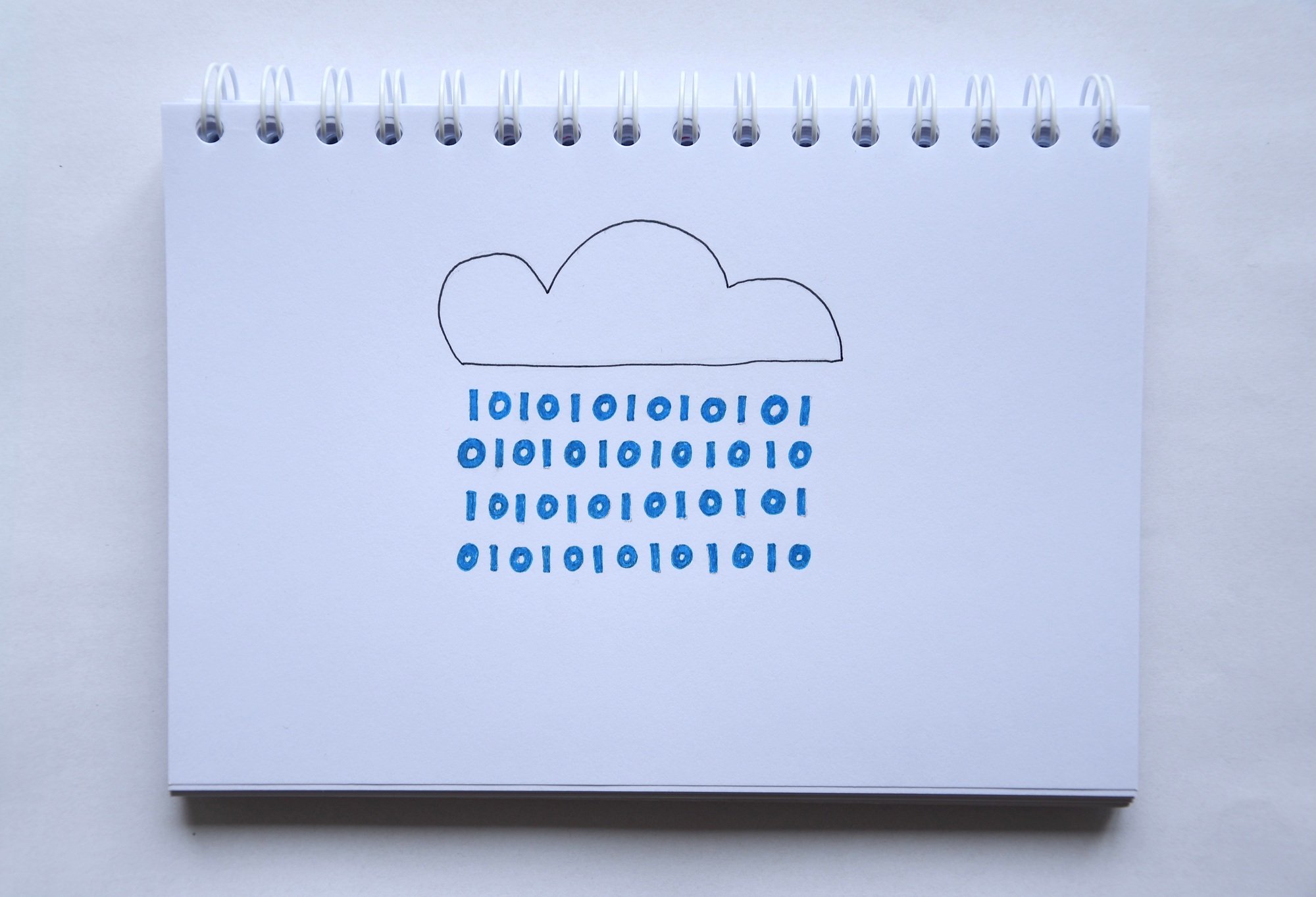 Overhead photo of a notebook with a drawing of a cloud from which rain in binary numbers fall