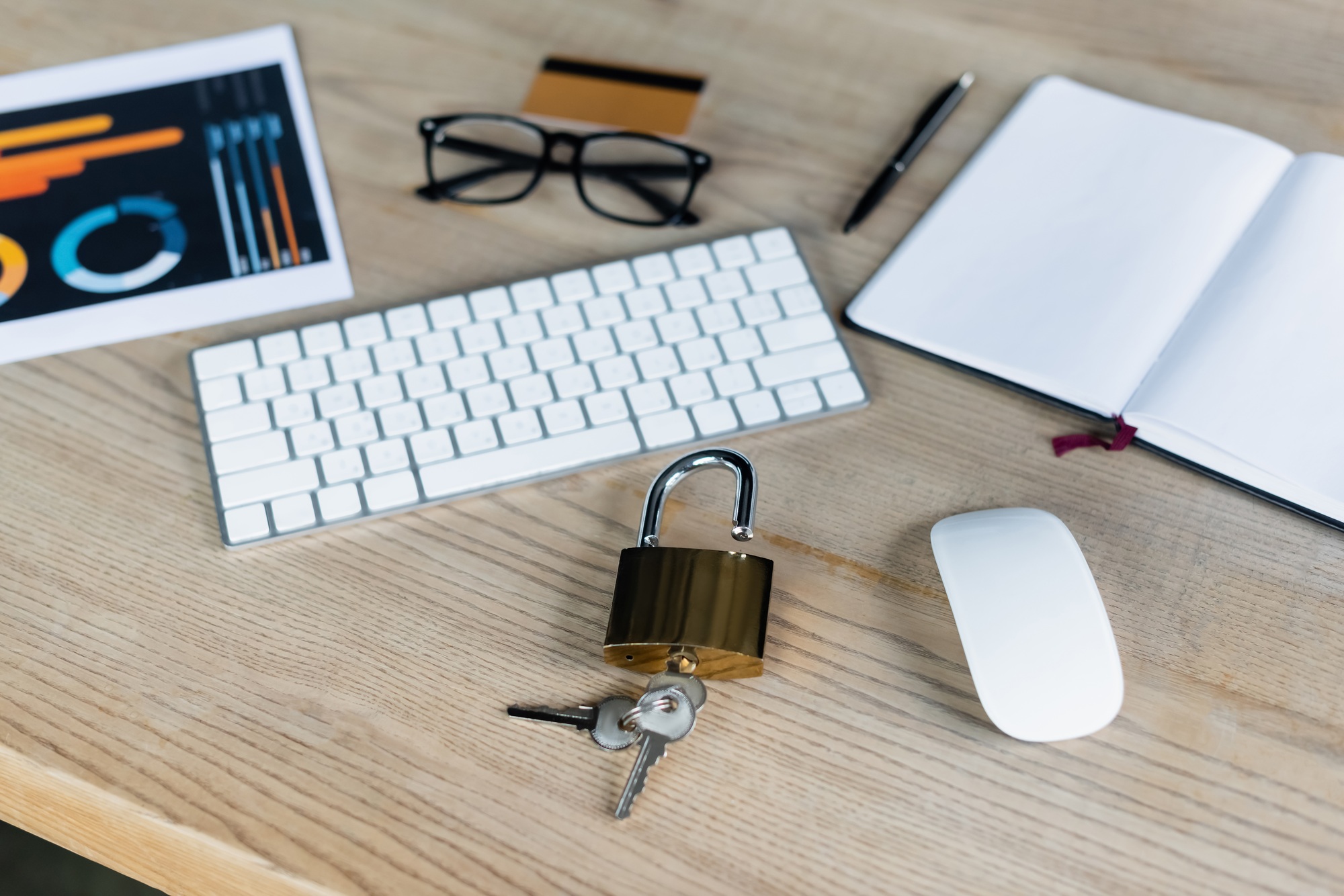 Padlock with keys near computer mouse, keyboard and notebook on table