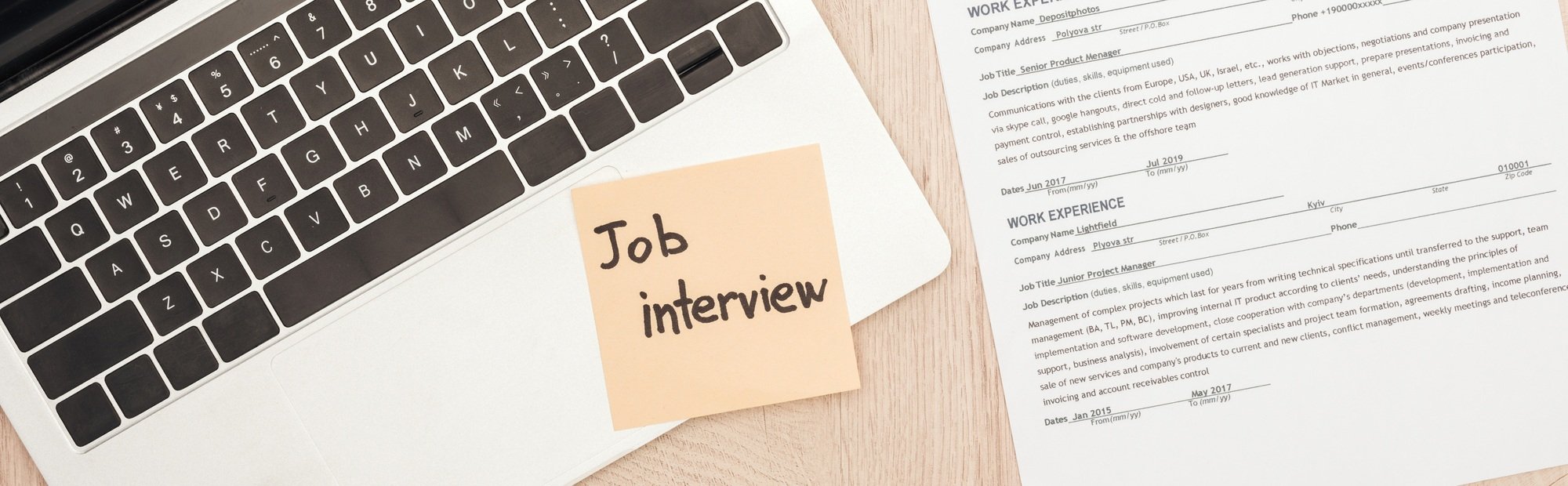 panoramic shot of laptop, resume template and sticky note with job interview lettering on wooden