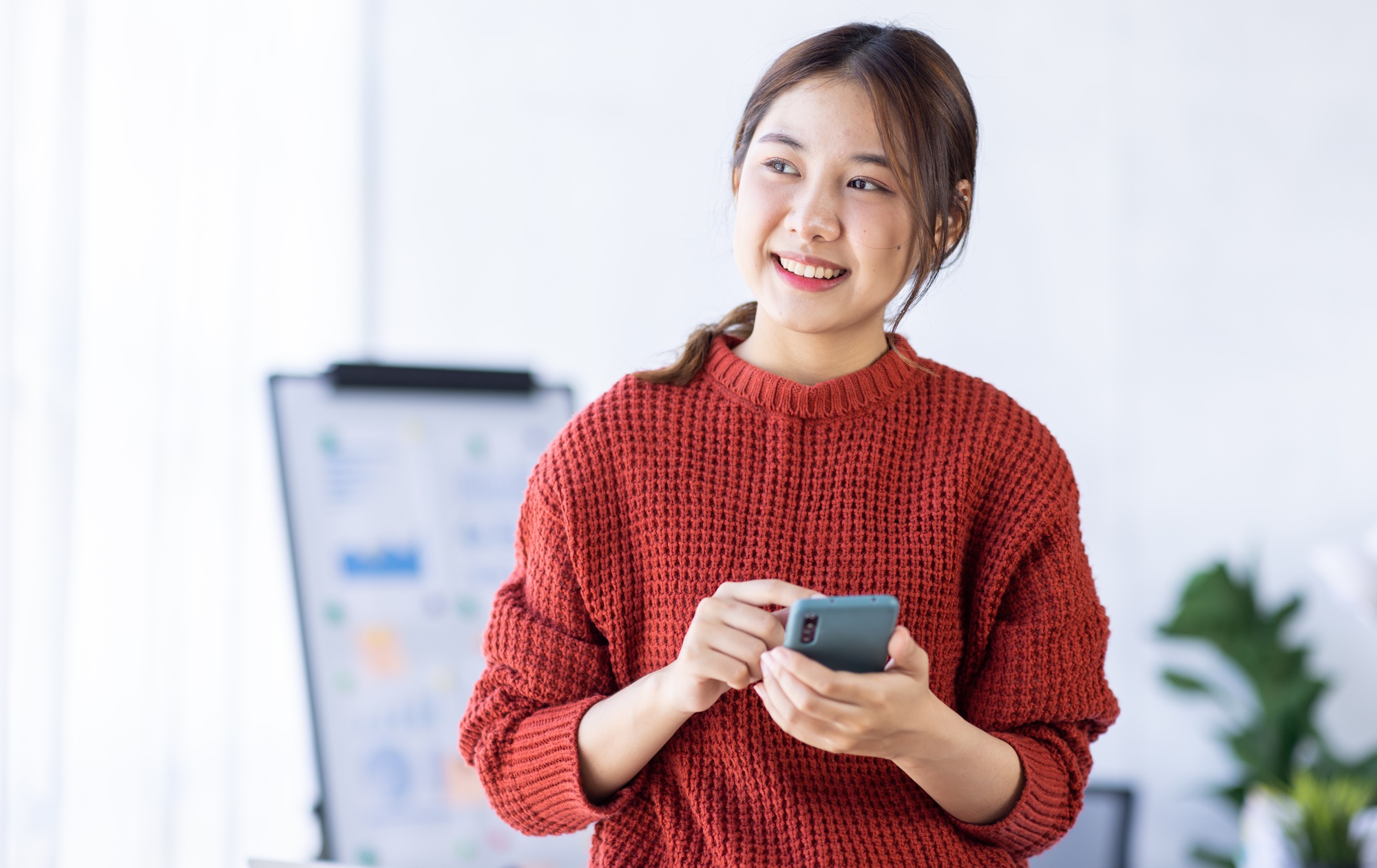 Portrait of a cheerful young business Asian woman using smartphone application in workplace office,