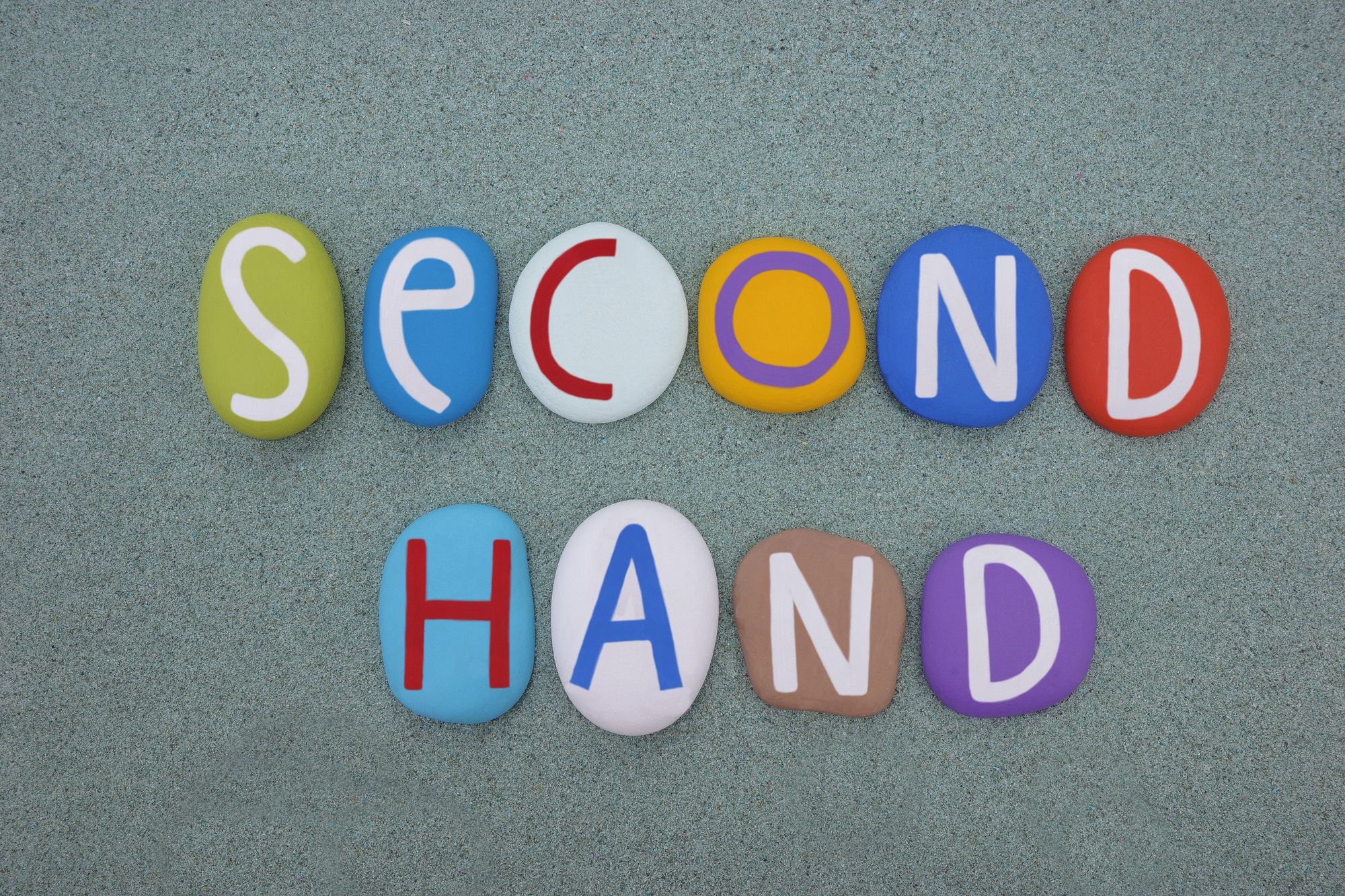 Second hand, creative logo composed with multi colored stone letters over green sand
