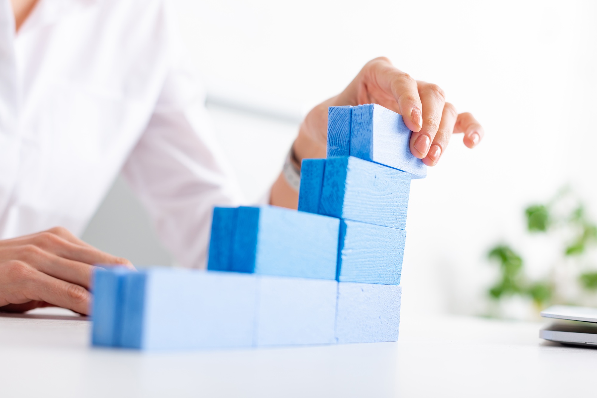 Selective focus of businesswoman making marketing pyramid with blue building blocks near laptop on