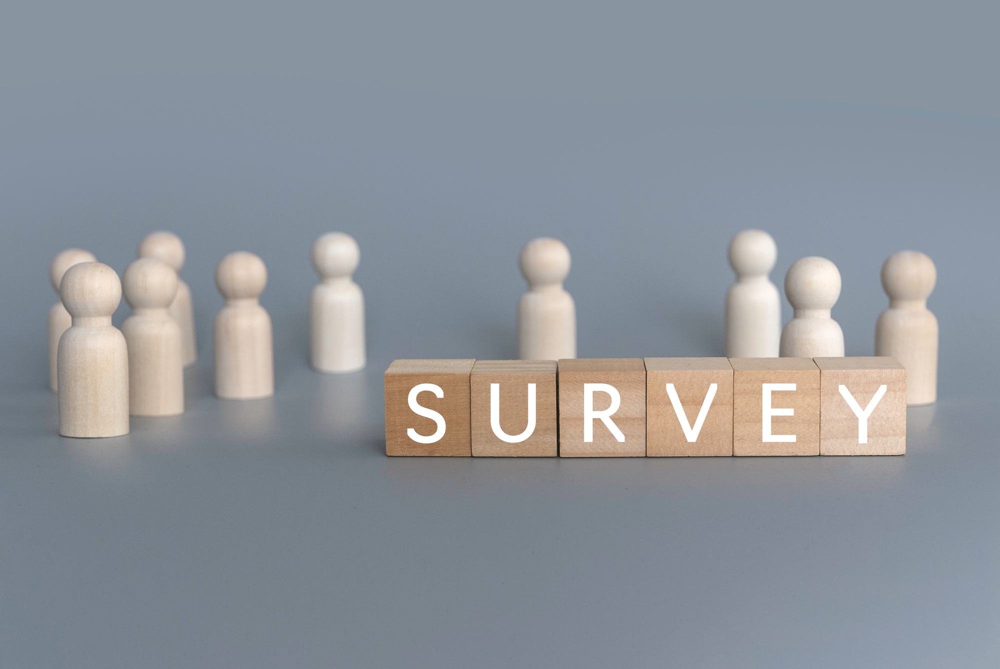 Selective focus of wooden people with a wooden cube written with Survey on gray background.