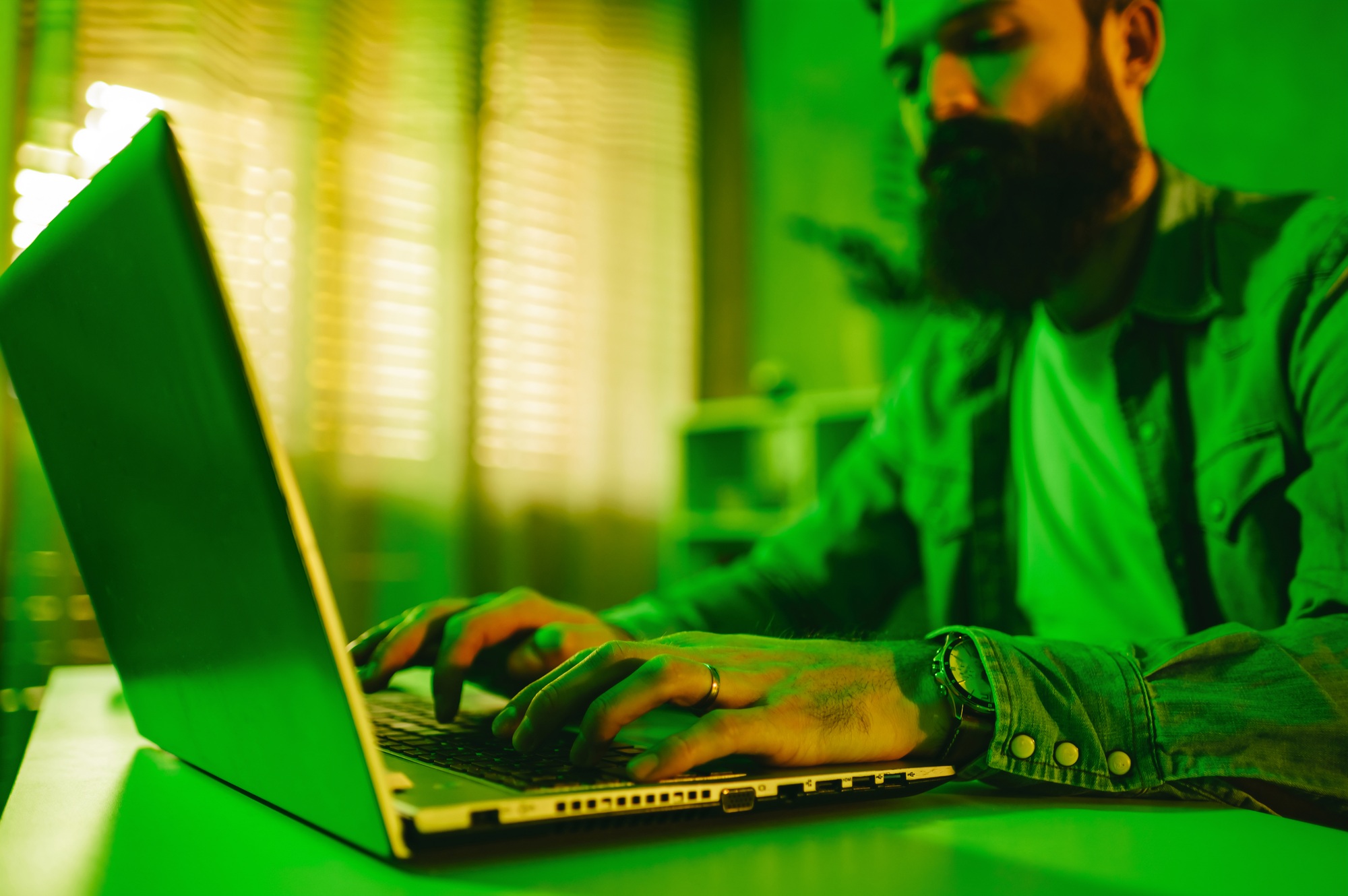 Selective focus on data entry expert typing on a keyboard in a green-lighted home office.