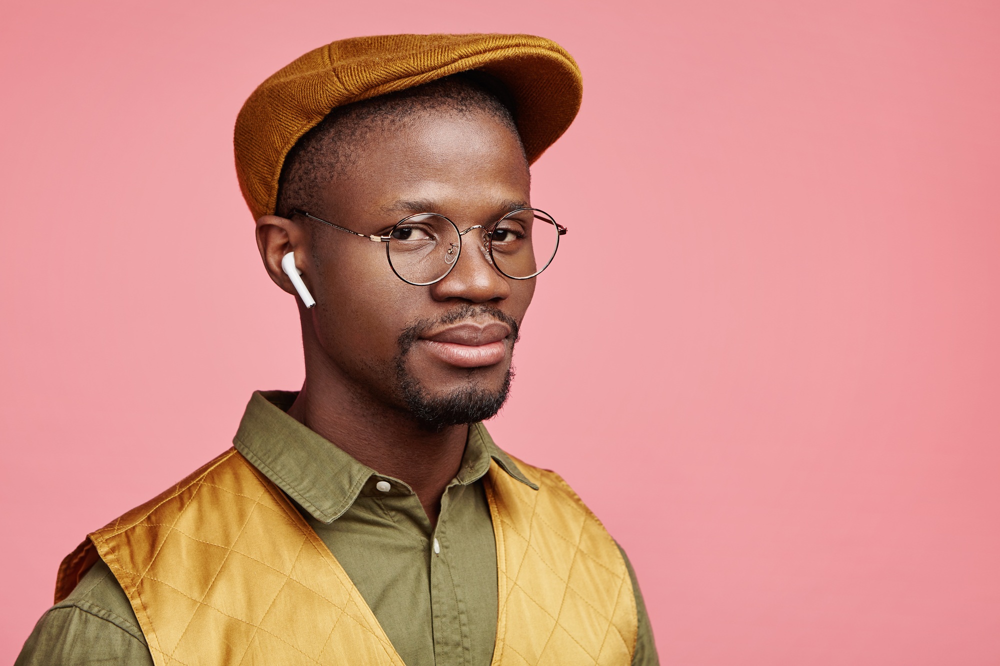 Serious dark skinned male listens music or news on radio website, uses modern wireless earphones, ad
