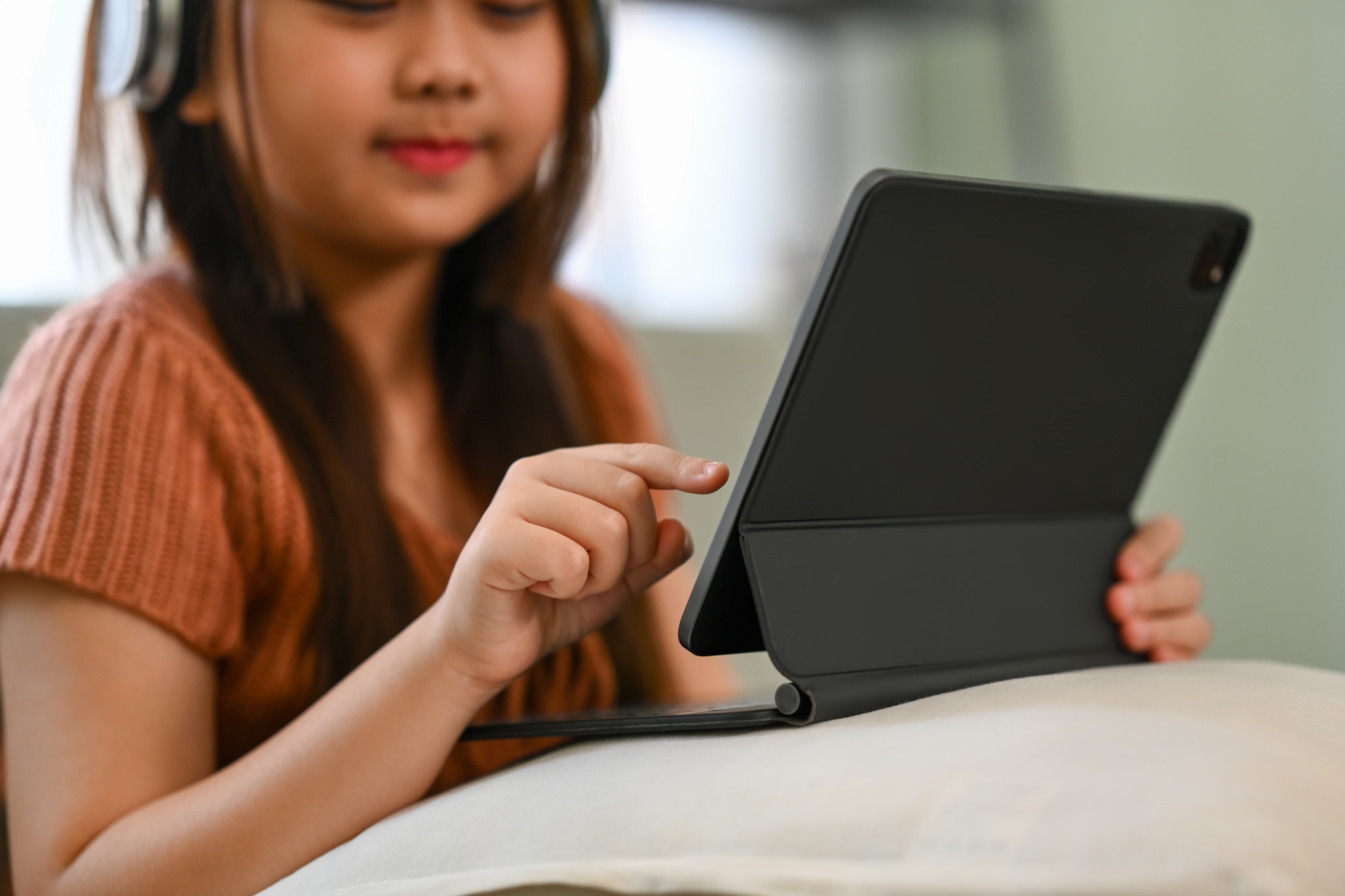 Smiling Asian girl in headphone studying virtual course with remote tutor at home.