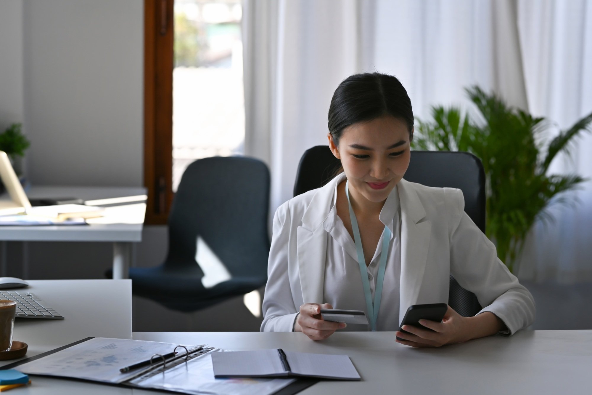 Smiling beautiful businesswoman holding credit card and shopping online with smart phone.