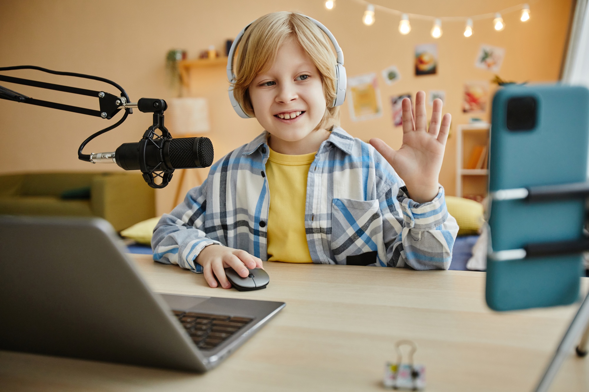 Smiling boy waving hand to online audience while making livestream