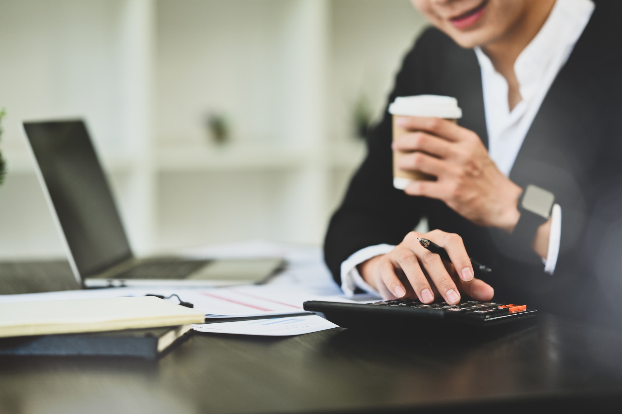 Smiling businessman drinking coffee and calculating tax income and expenses at workplace