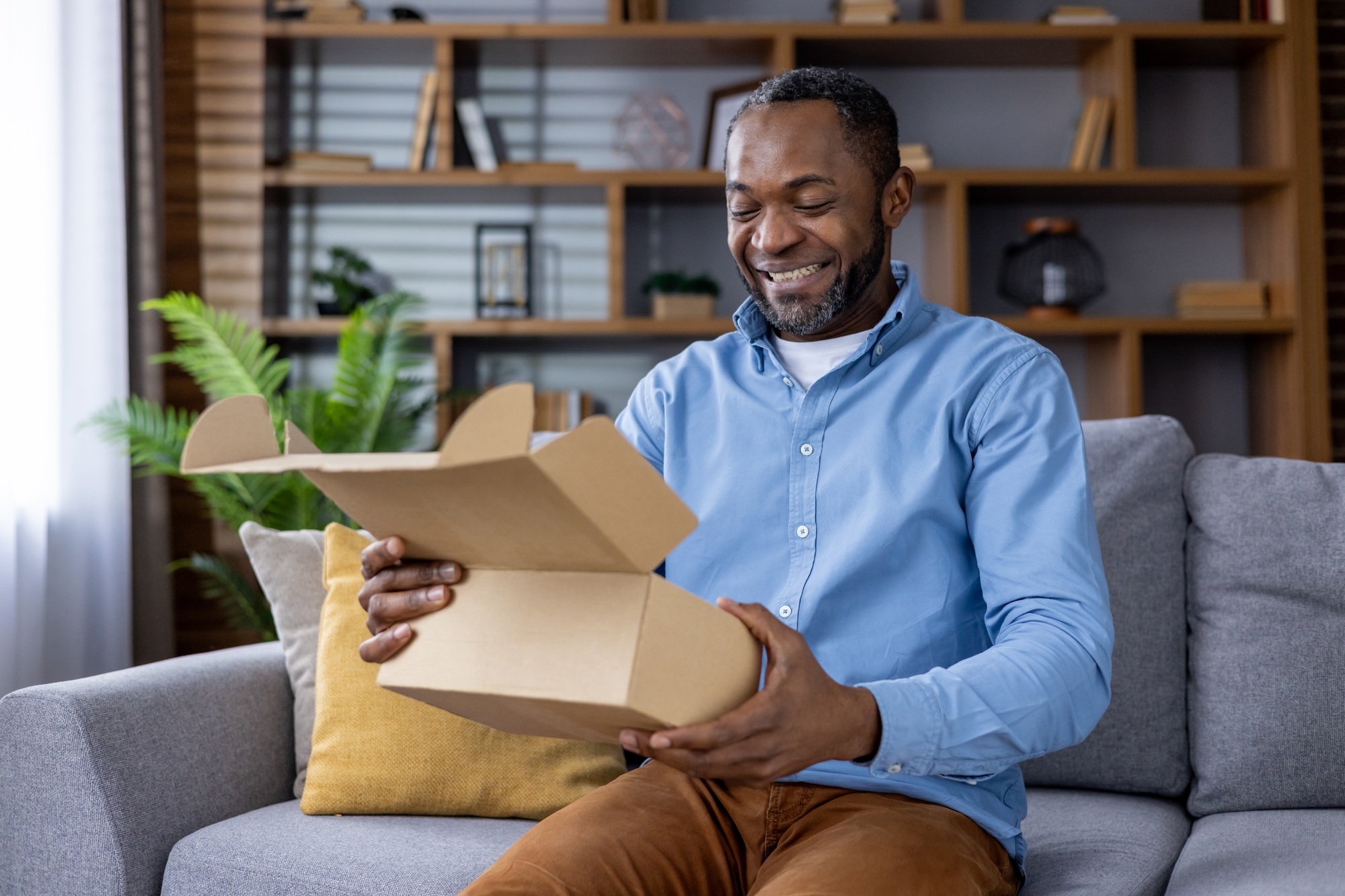 Smiling man unboxing a package while sitting on a couch at home