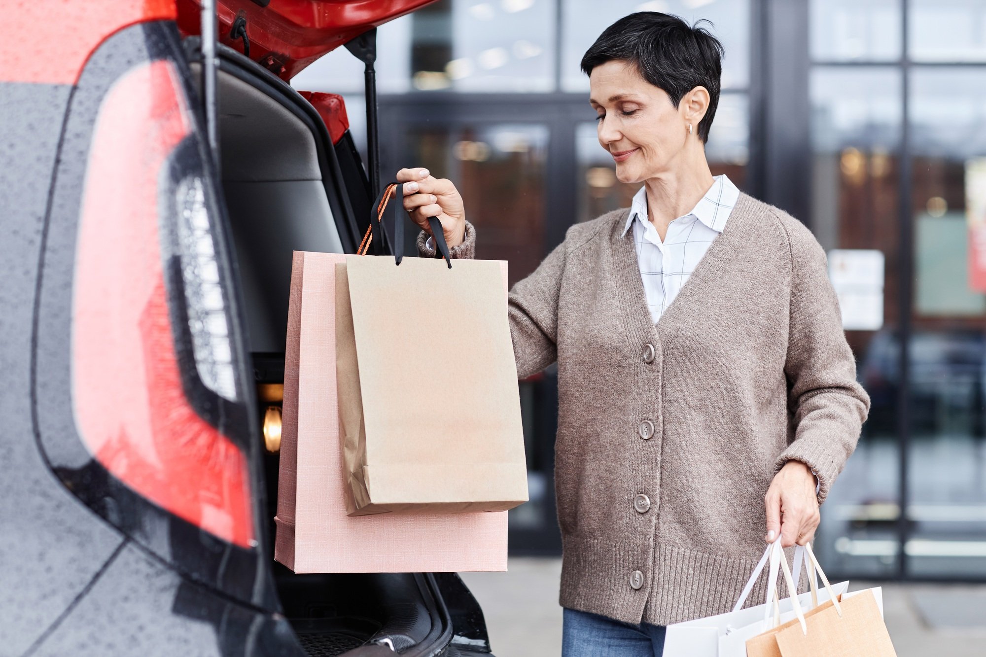 Smiling woman putting shopping bags on car trunk outdoors in parking lot
