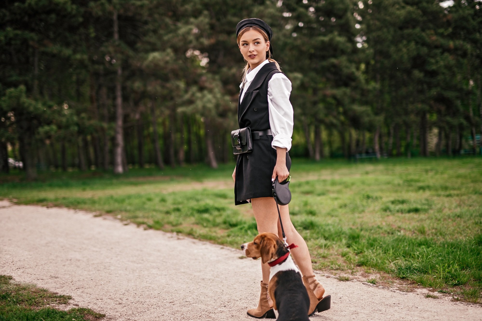 Stylish woman with dog walking on park alley