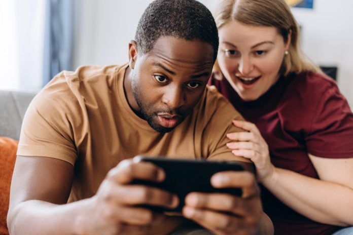 Surprised multiracial coupe looking at smartphone screen, received online lottery win message