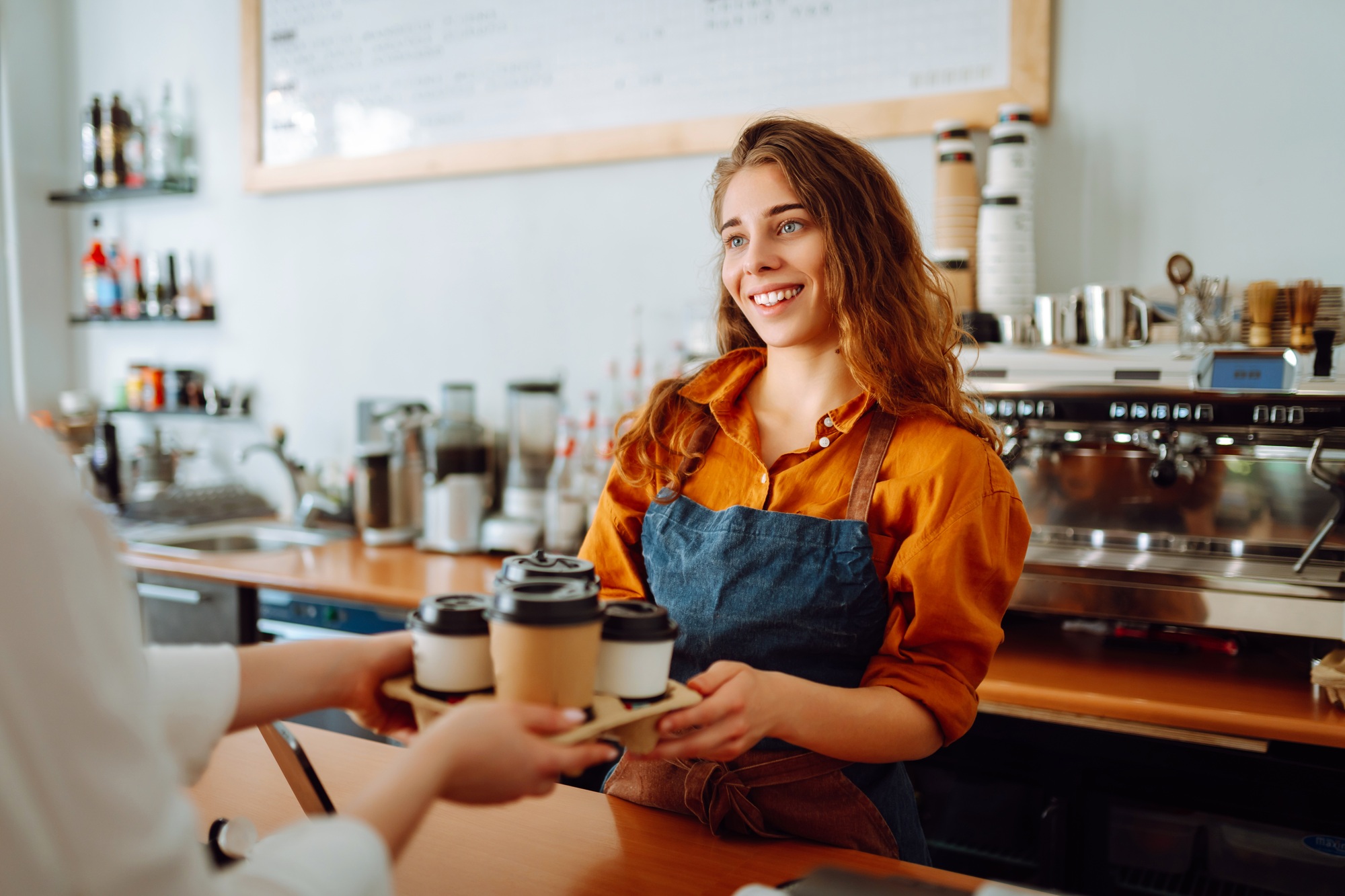Takeaway food concept. A beautiful female barista gives to-go coffee to a client. Business concept.